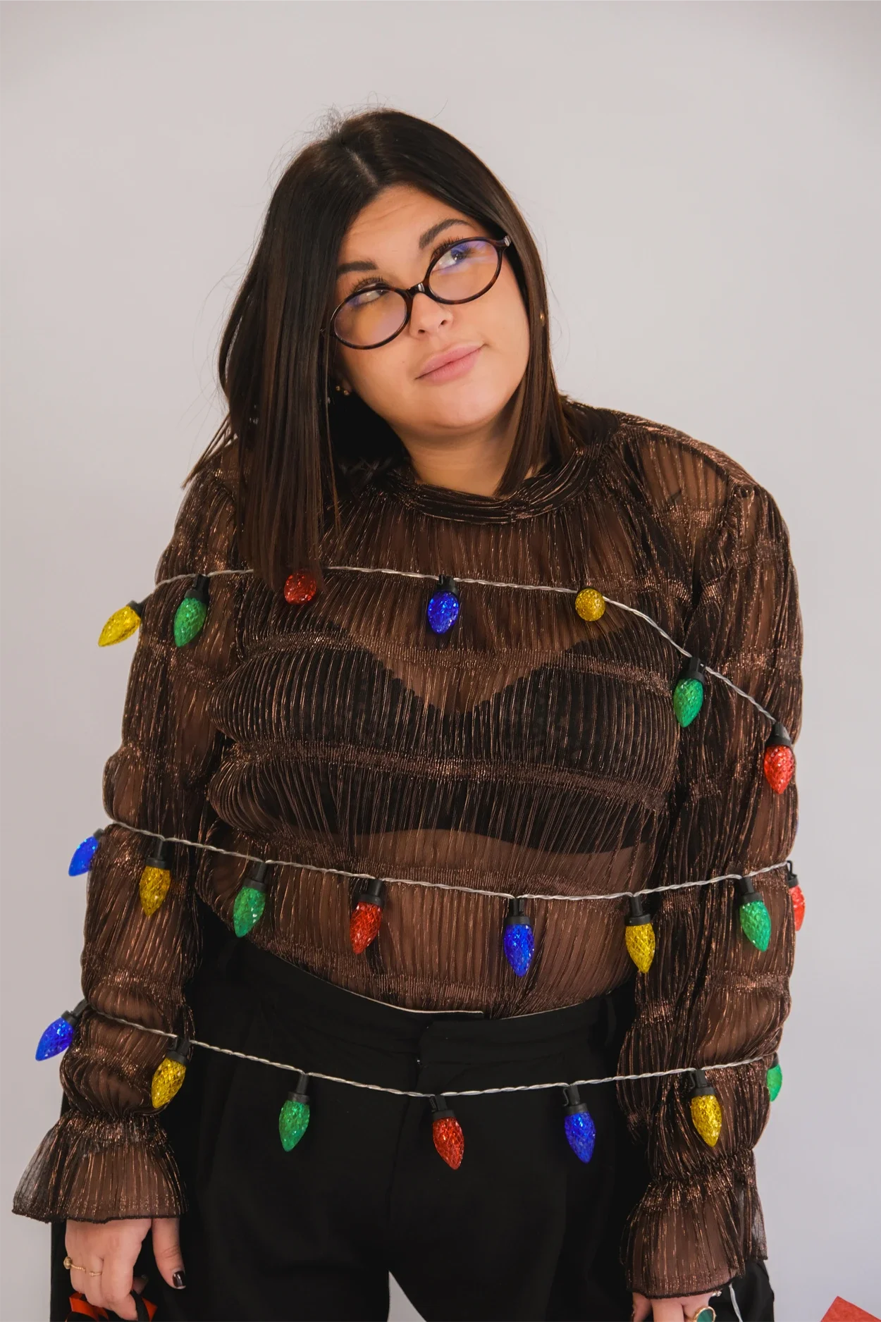 Une femme portant un haut en tissu transparent à rayures avec des guirlandes de lumières de Noël colorées entremêlées, look décontracté.