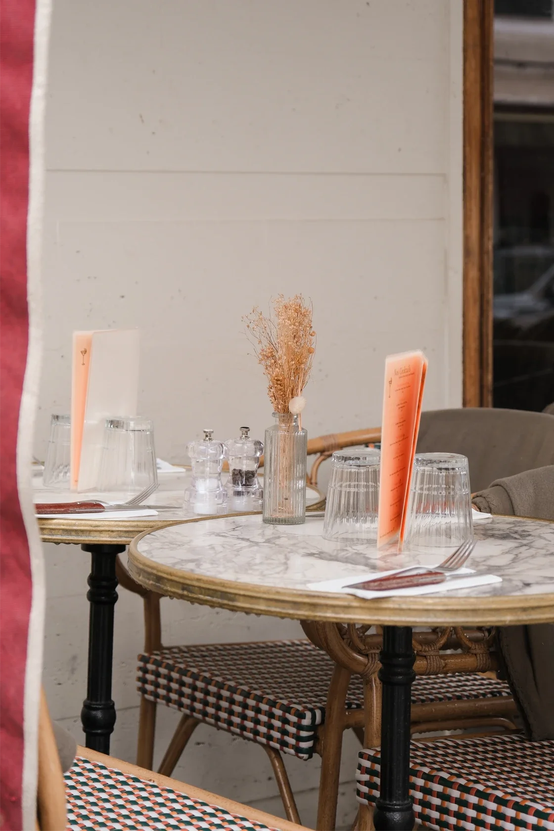 Une table de restaurant avec une nappe en marbre, des verres, des assiettes, des couverts, une petite bouteille de sel et poivre, une décoration florale et des menus.