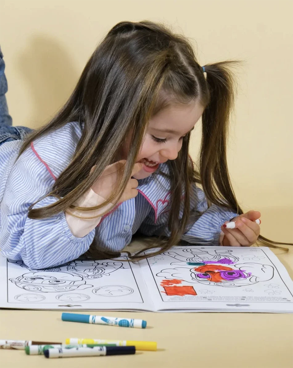 Une fille qui colorie un dessin avec des marqueurs, portant un pyjama rayé. Elle sourit en regardant son coloriage.