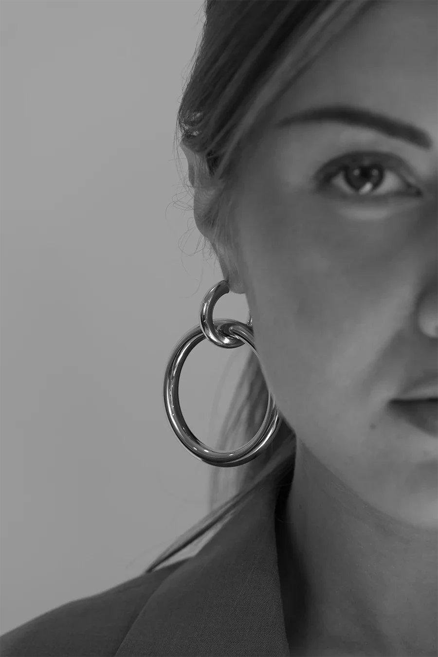 Détail noir et blanc du visage d'une femme portant une grosse boucle d'oreille en acier, mettant en valeur un œil, le sourcil et une partie du visage avec une expression neutre.