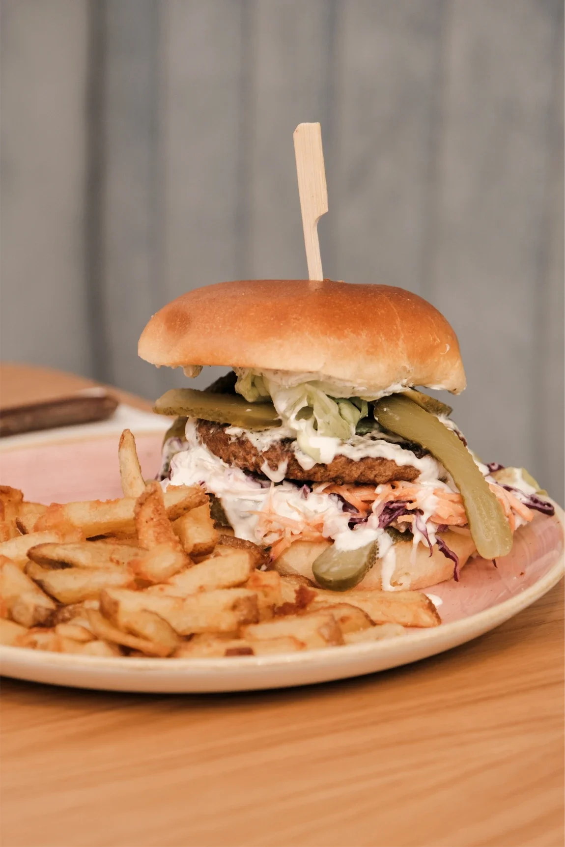 Un burger garni de légumes, une sauce blanche, de la viande, des cornichons, du chou, et une boule de pain, accompagné de frites.