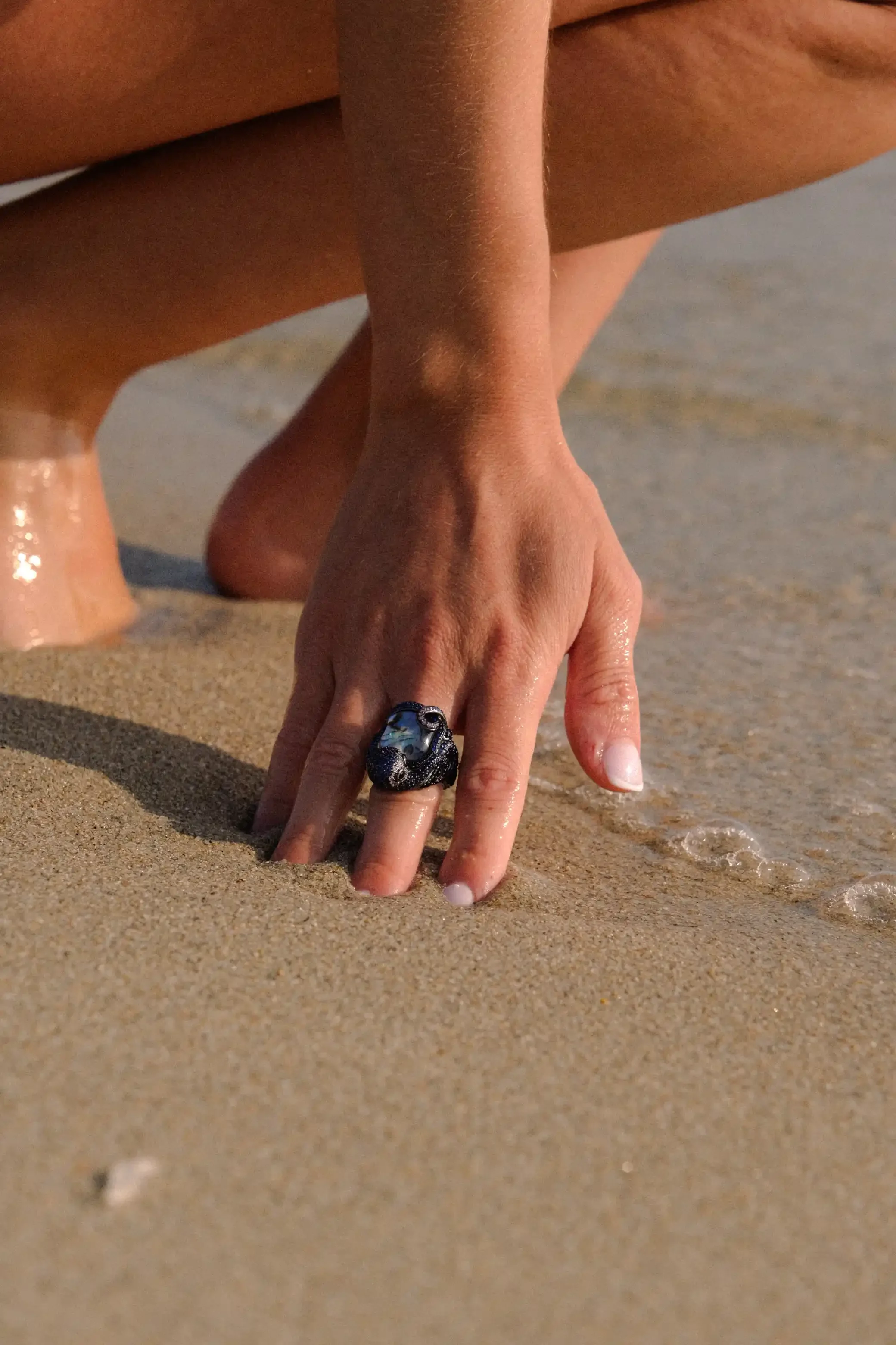 Main d'une personne portant une bague, touche le sable d'une plage, avec l'eau qui arrive.