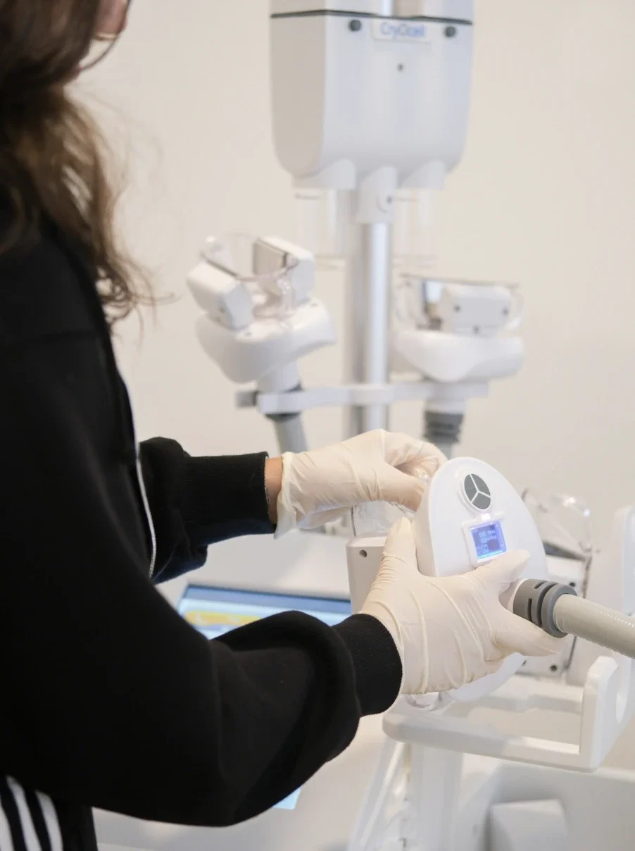 Une personne portant des gants examine un appareil médical dans un laboratoire ou un centre médical. En arrière-plan, il y a des équipements médicaux en blanc.