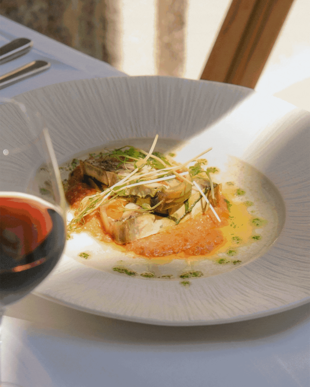 Plat de poisson avec sauce et garniture, servi dans une assiette blanche, avec un verre de vin rouge à côté.