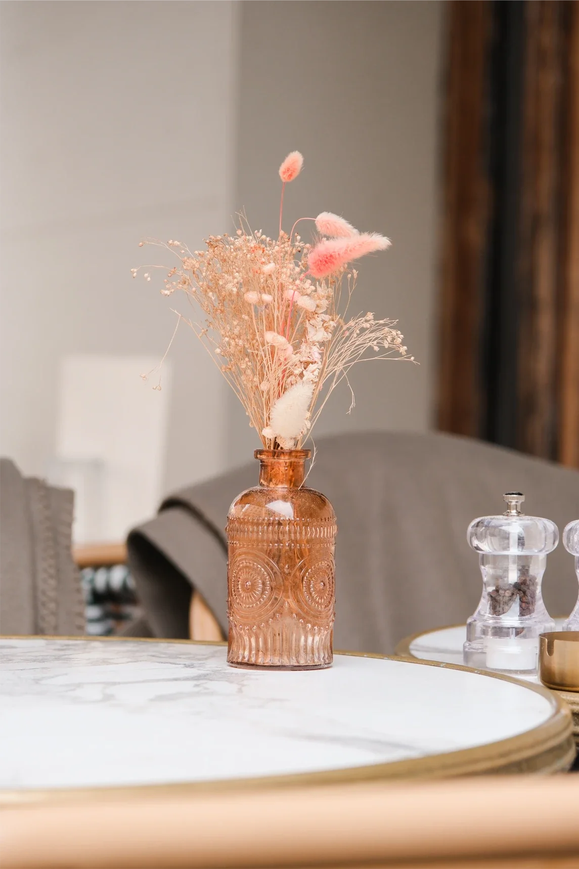 Vase en verre orange contenant des fleurs séchées roses, blanches et beiges, placé sur une table en marbre blanc avec bord en bois