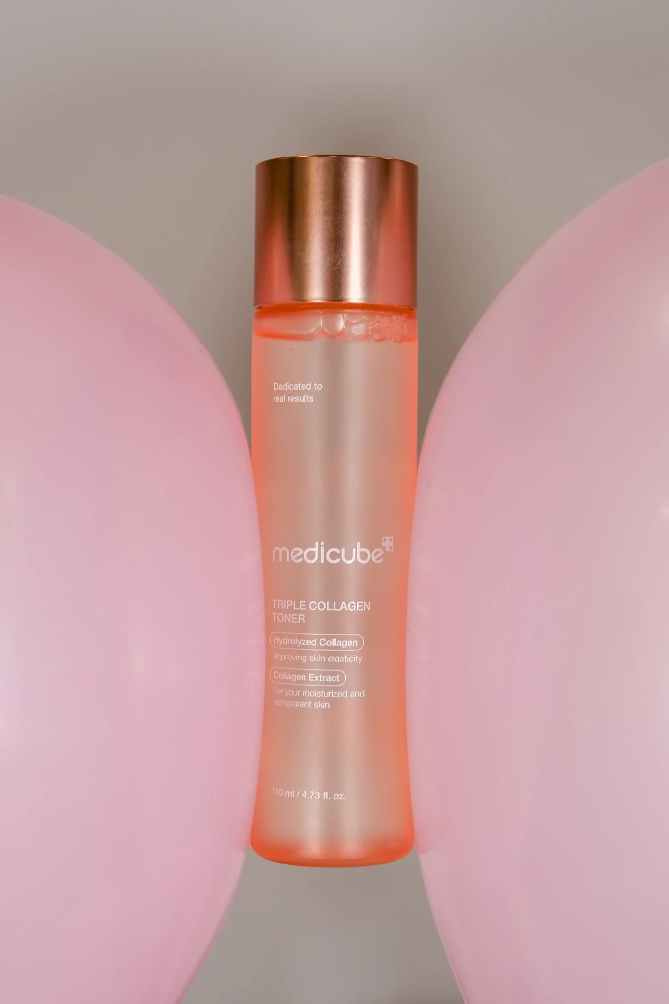 Une bouteille de tonique à la molécule de collagène, avec un bouchon en or rose, posée entre deux mains de couleur rose pastel.