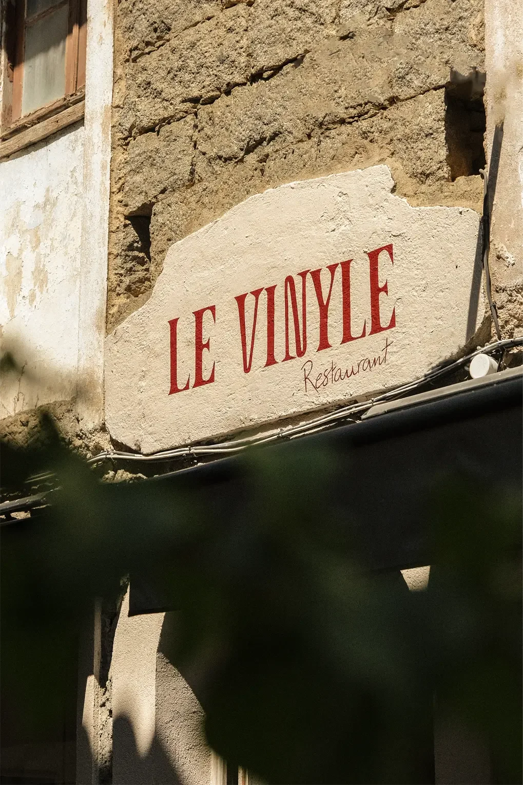Panneau indiquant 'LE VIOULE Restaurant' fixé sur un mur en pierre, avec une fenêtre en bois à gauche.