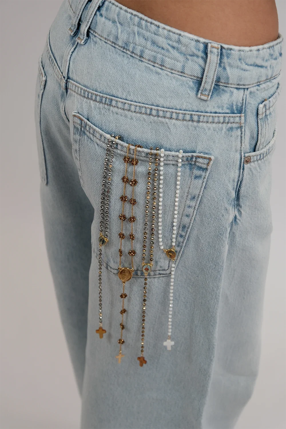 Pantalon en jeans clair avec plusieurs chaînes de bijoux or et argent accrochées à la poche arrière.