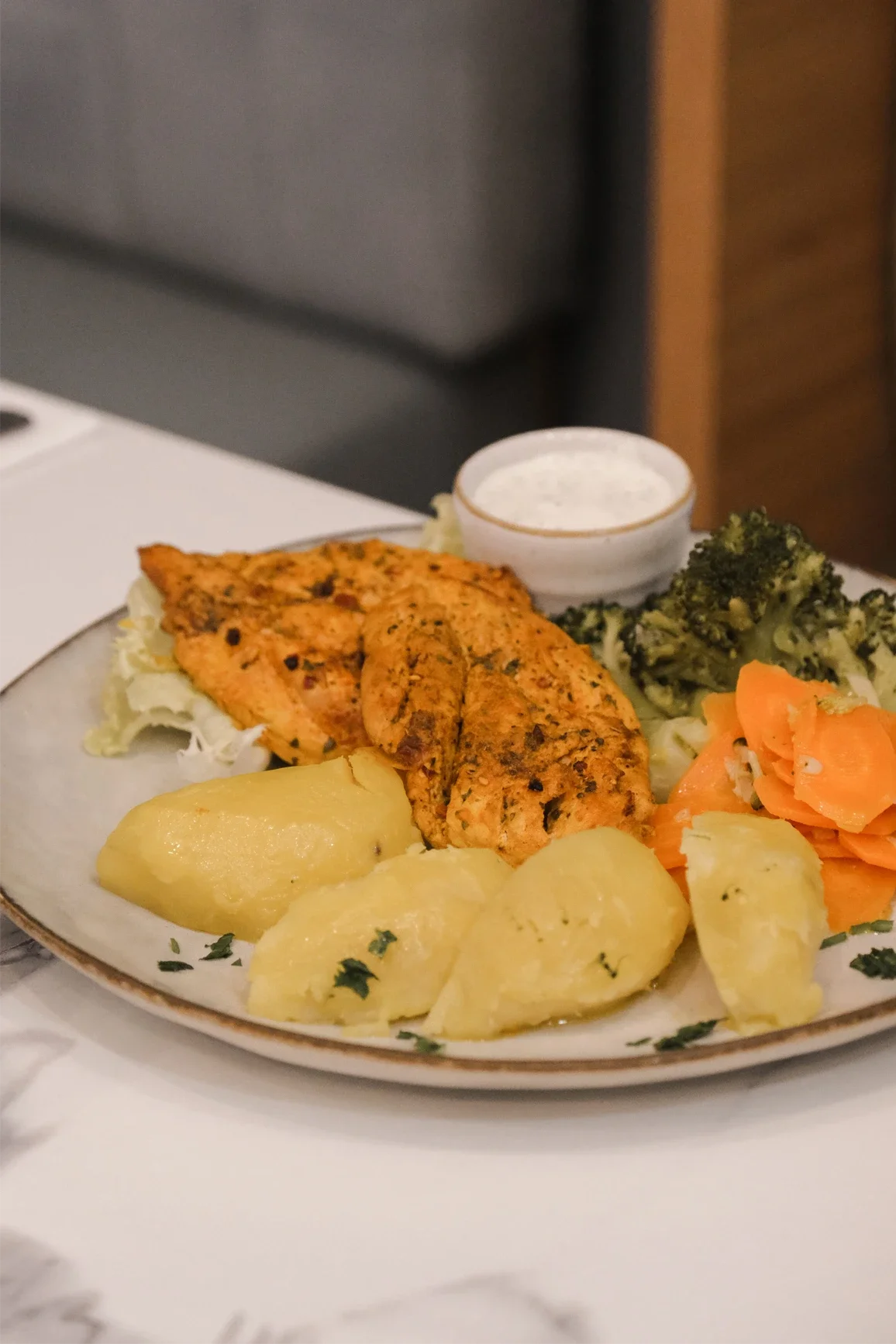 Assiette de nourriture indienne comprenant du poulet tandoori, des pommes de terre, des légumes broccoli et carottes, et une sauce au yaourt.