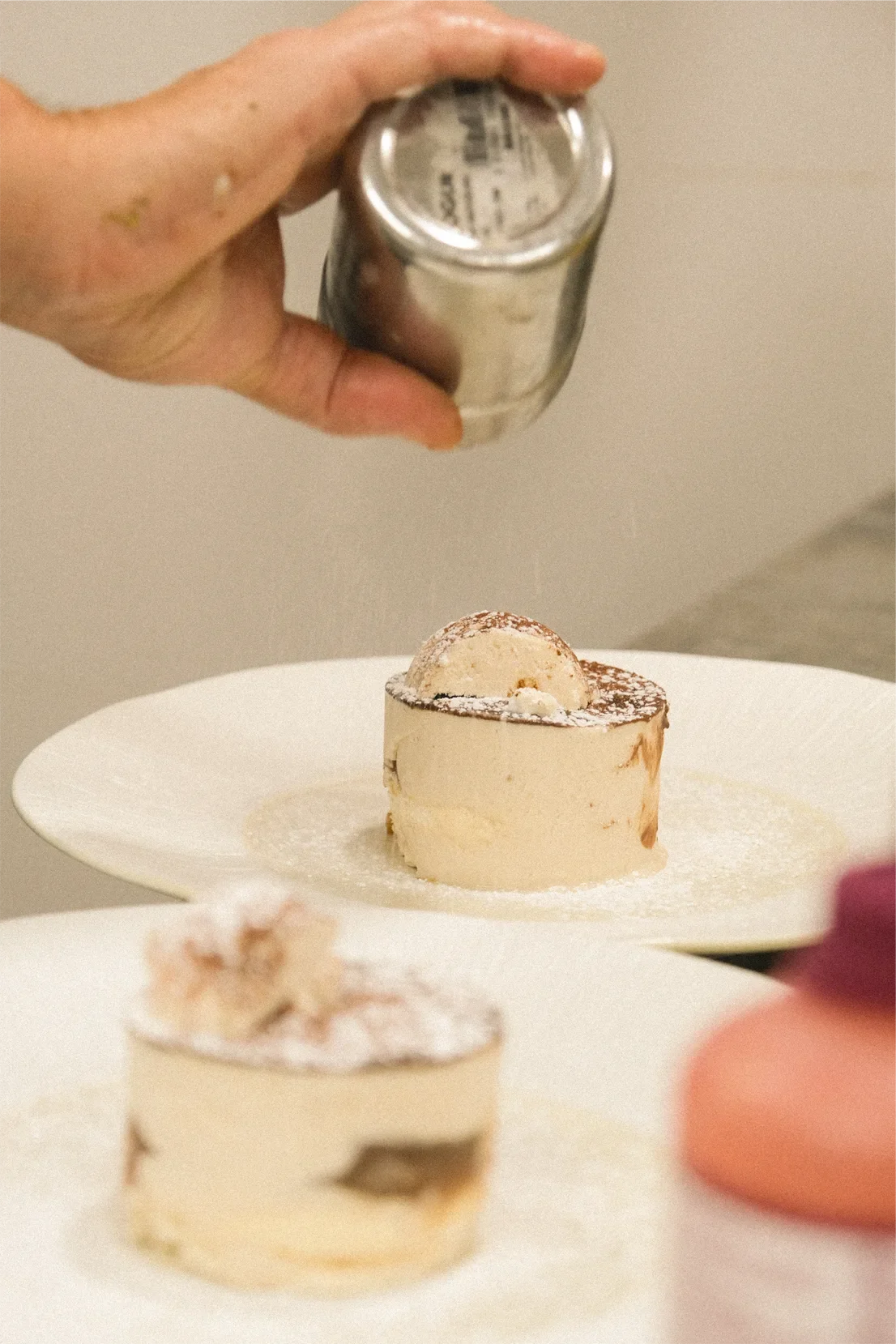 Une main saupoudre du sucre glace sur une tarte au citron meringuée, avec une autre tarte visible au premier plan.