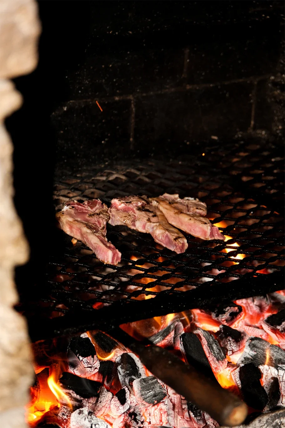 De la viande en train de griller sur un barbecue avec des braises en dessous.