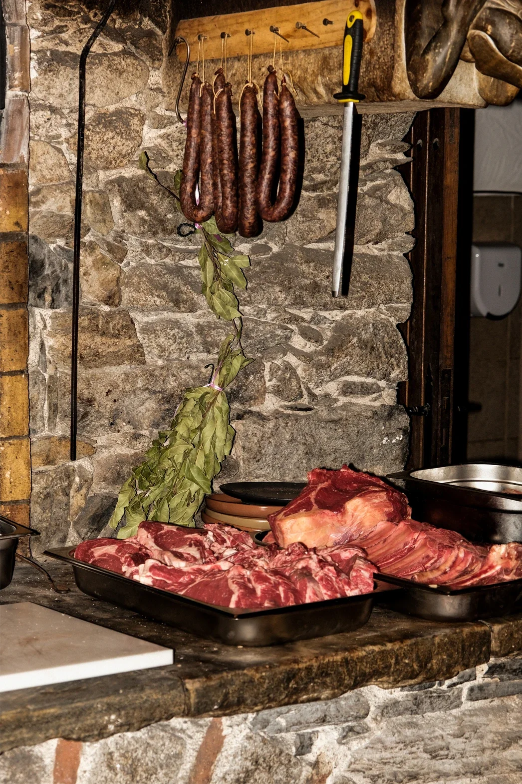 Viandes en gros morceaux et saucisses suspendues, herbes séchées, ustensiles et vaisselle en cuisine rustique.