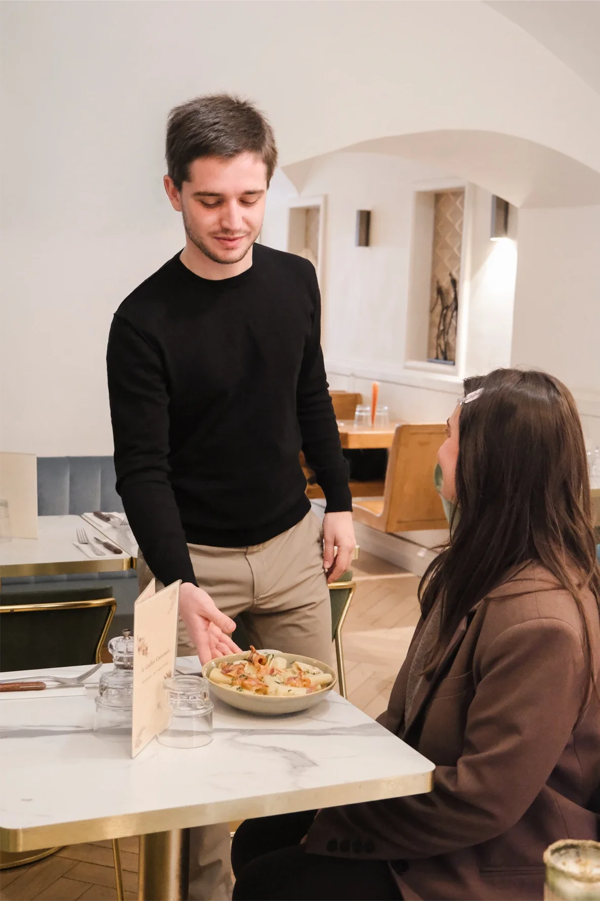 Un homme sert une pizza à une femme assise à une table dans un restaurant.