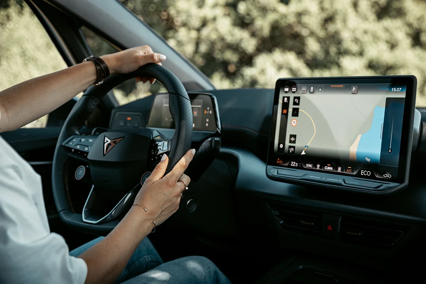 L'intérieur d'une voiture électrique avec un dashboard numérique affichant une carte de navigation et un volant avec un logo de voiture sportive