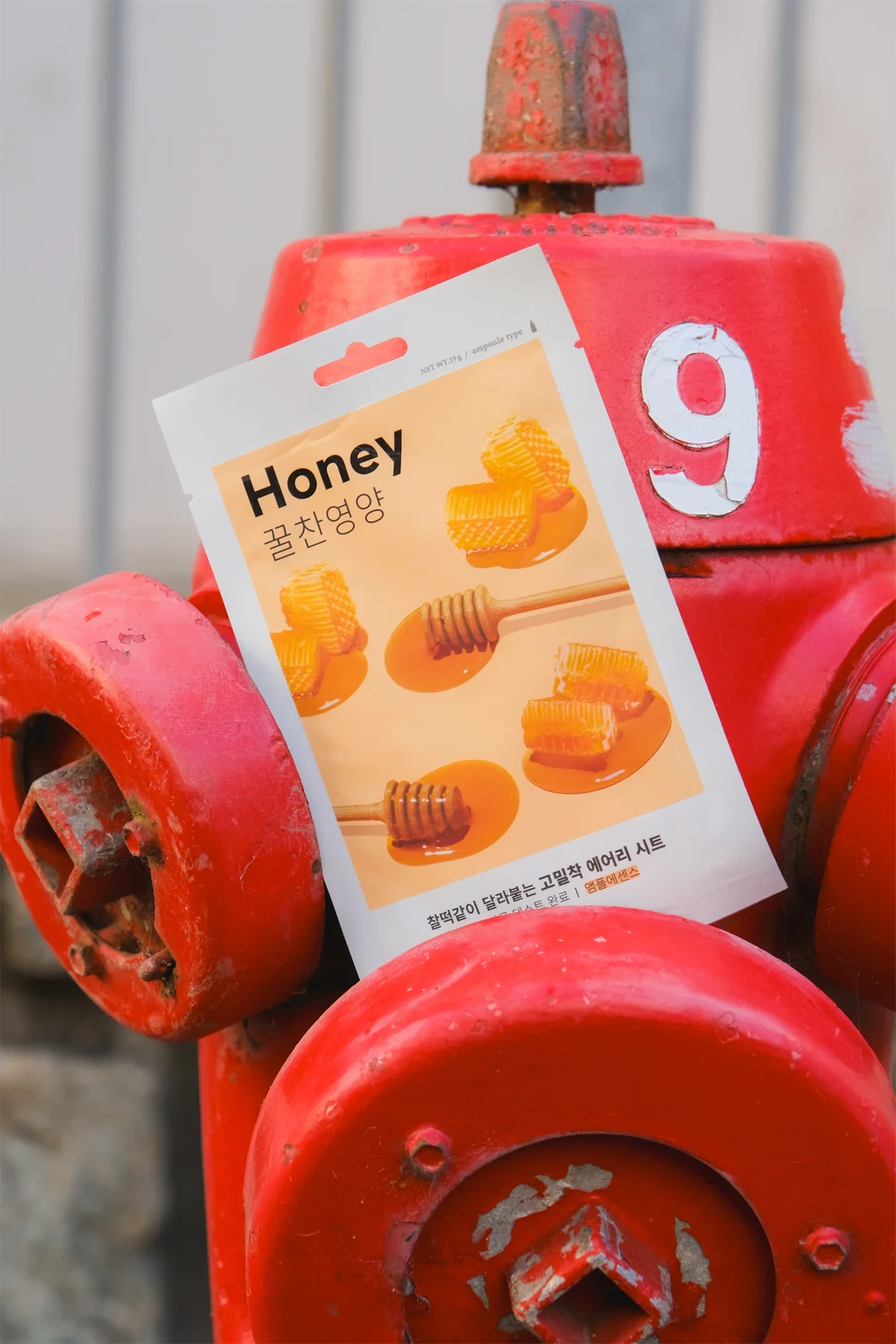 Une affiche promotionnelle pour du miel Honey, affichée sur une borne d'incendie rouge en métal rouillé.