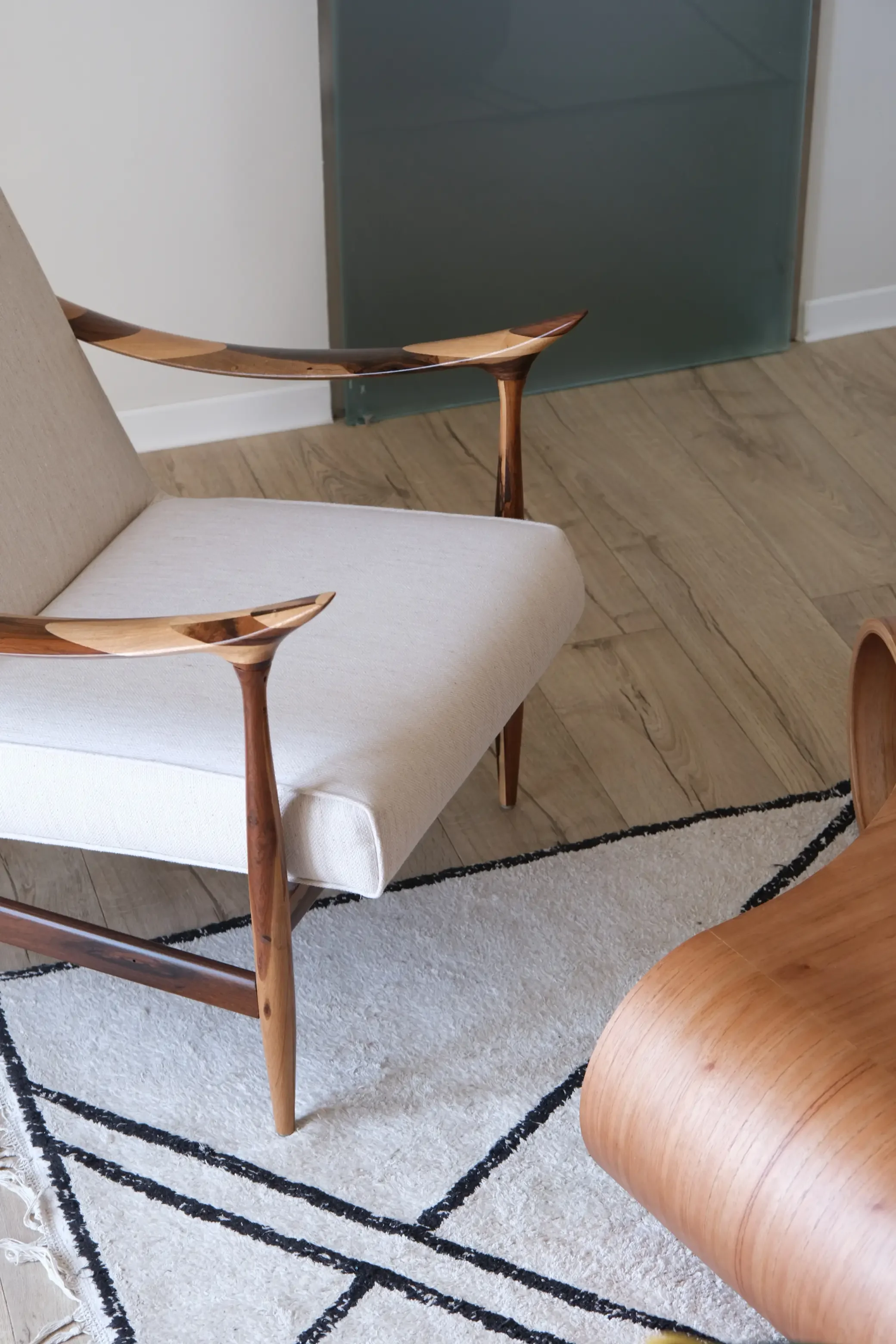 Intérieur d'une pièce avec une chaise en bois clair et tissu beige, un tapis blanc avec des bandes noires, un mur blanc et un panneau en verre opaque vert