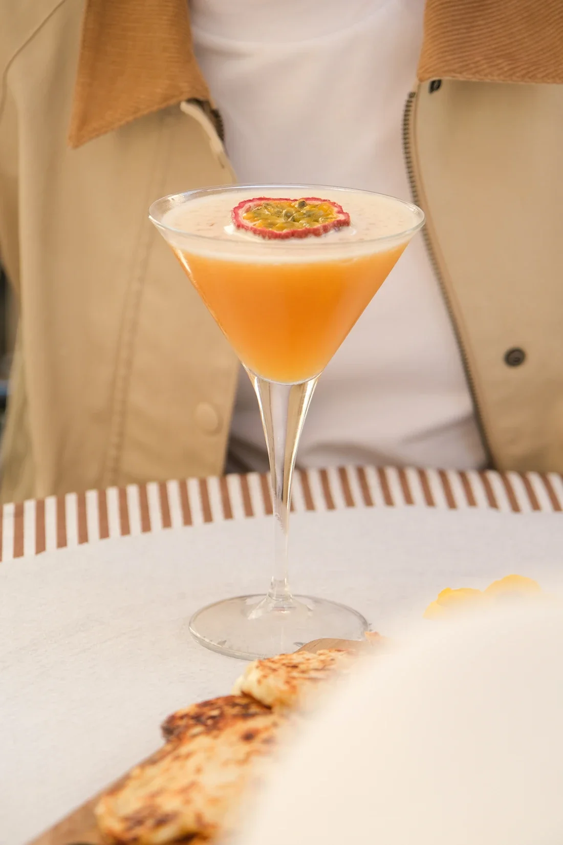Un cocktail orange dans un verre à martini, garni d'une tranche de fruit de la passion sur le dessus.