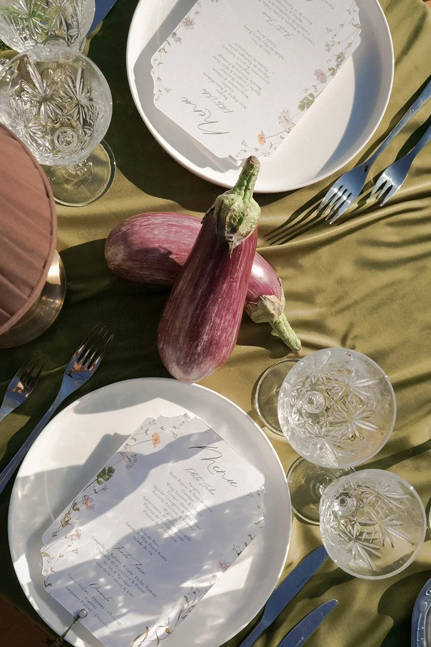 Table dressée pour un dîner avec des légumes courgettes, des assiettes, des verres à vin et des fourchettes, une carte de menu écrite en français