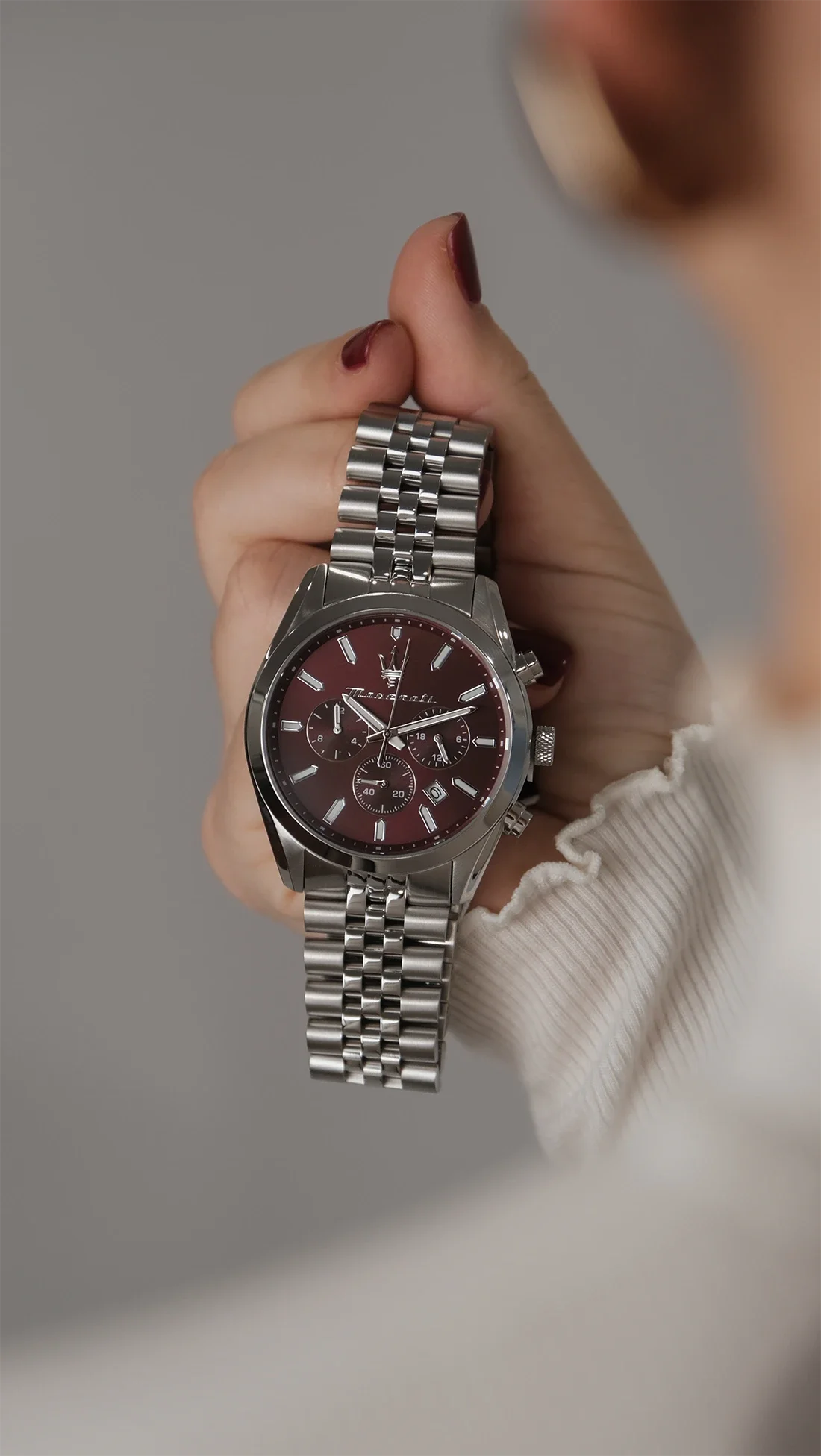 Une personne tient une montre-bracelet en acier inoxydable avec un cadran rouge foncé et plusieurs sous-cadrans