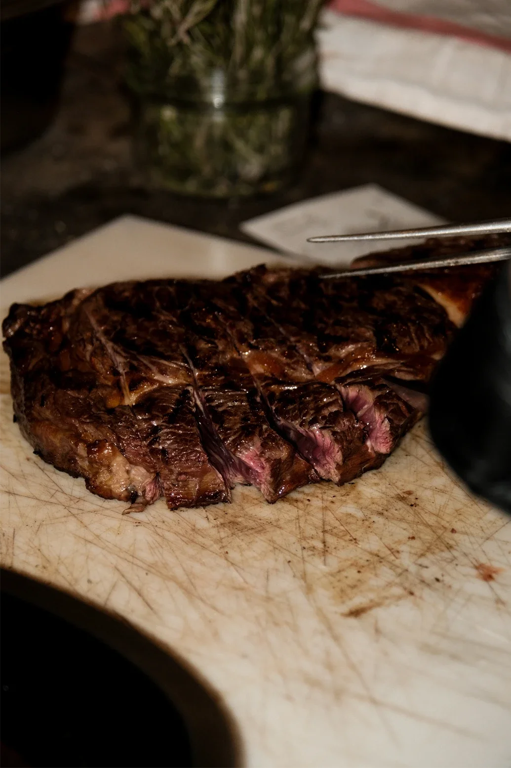 Une pièce de viande cuite, probablement un steak, sur une planche à découper en bois, avec un fond flou.