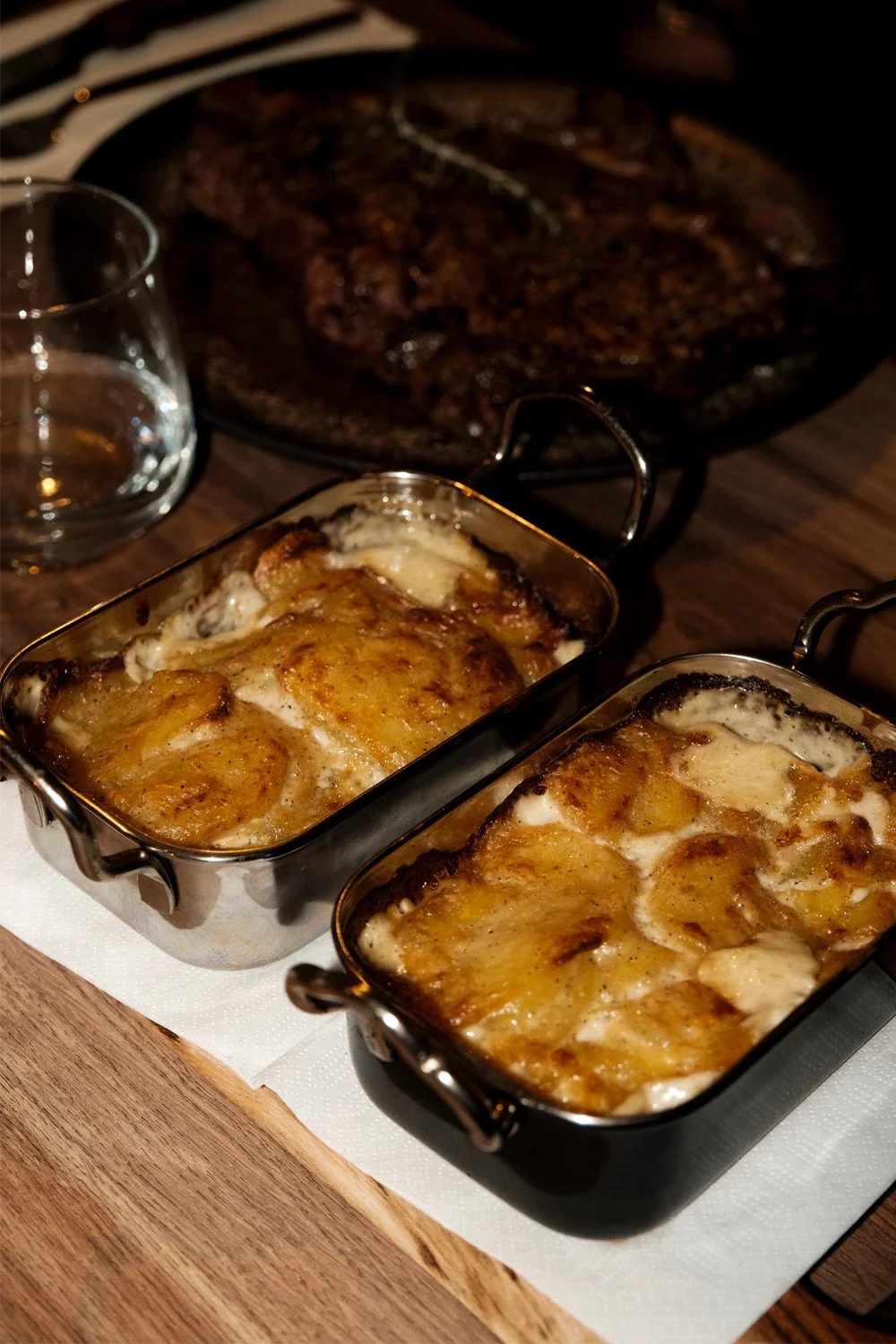 Deux plats de gratin au fromage avec une viande en arrière-plan sur une table en bois