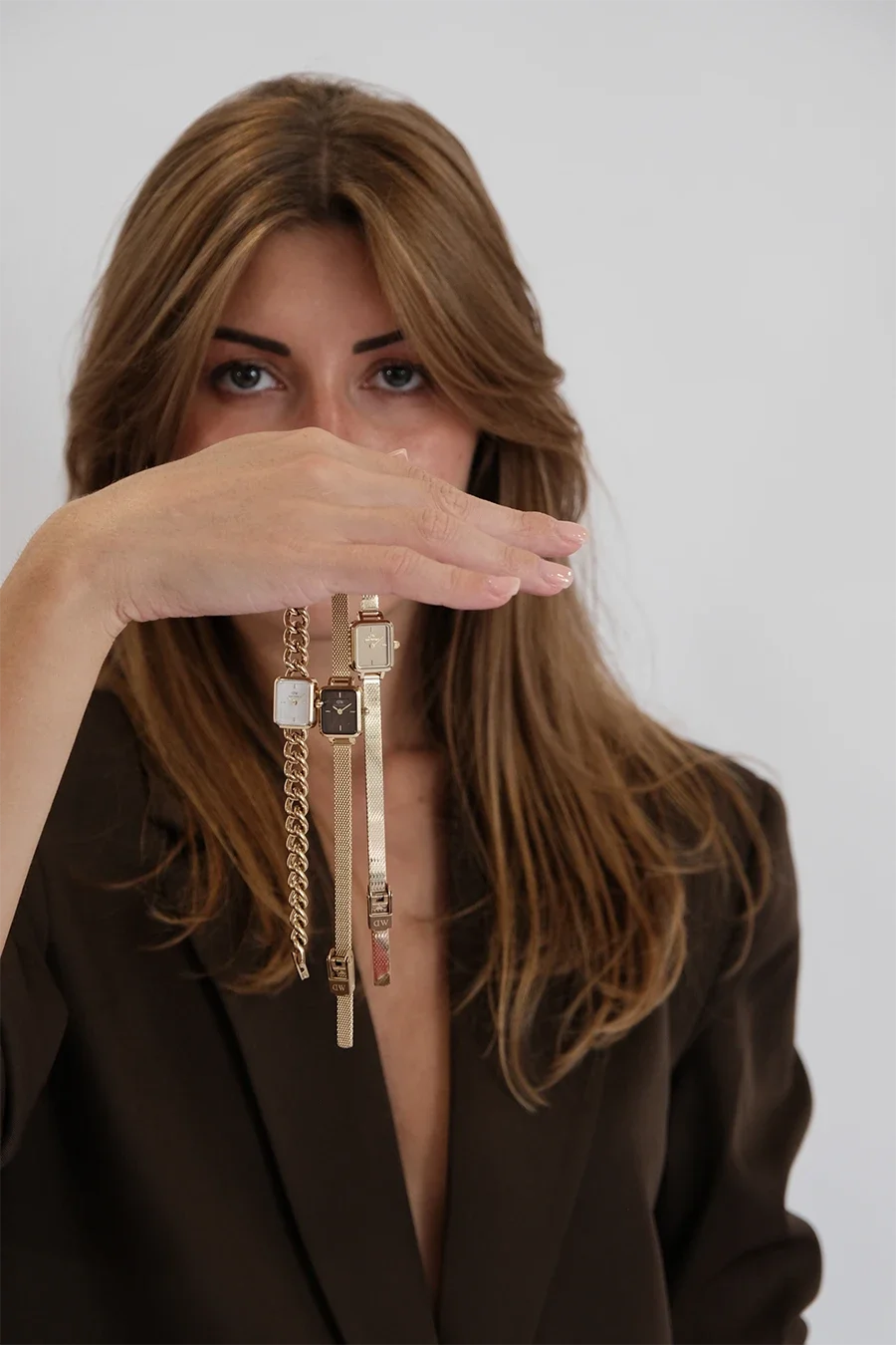 Une femme aux cheveux longs et bruns tient plusieurs montres élégantes pendues à sa main levée.
