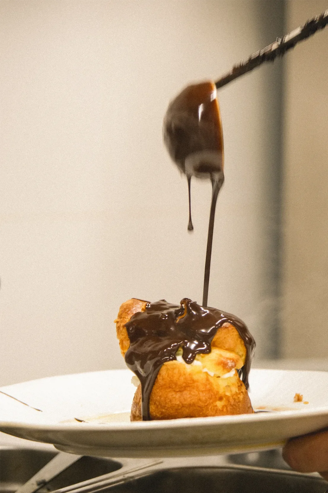 Une pâtisserie, probablement un chou, garnie de crème et recouverte de sauce au chocolat, est en train d'être décorée avec de la sauce au chocolat vers le haut.