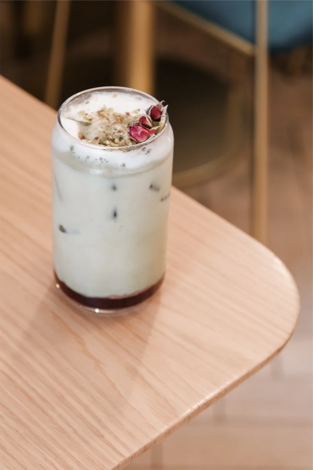 Un verre avec une boisson mousseuse blanche, garnie de pétales de roses séchées et de graines