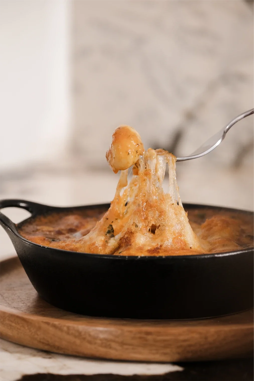 Gratin de pommes de terre avec fromage fondu dans une poêle noire sur une planche en bois.