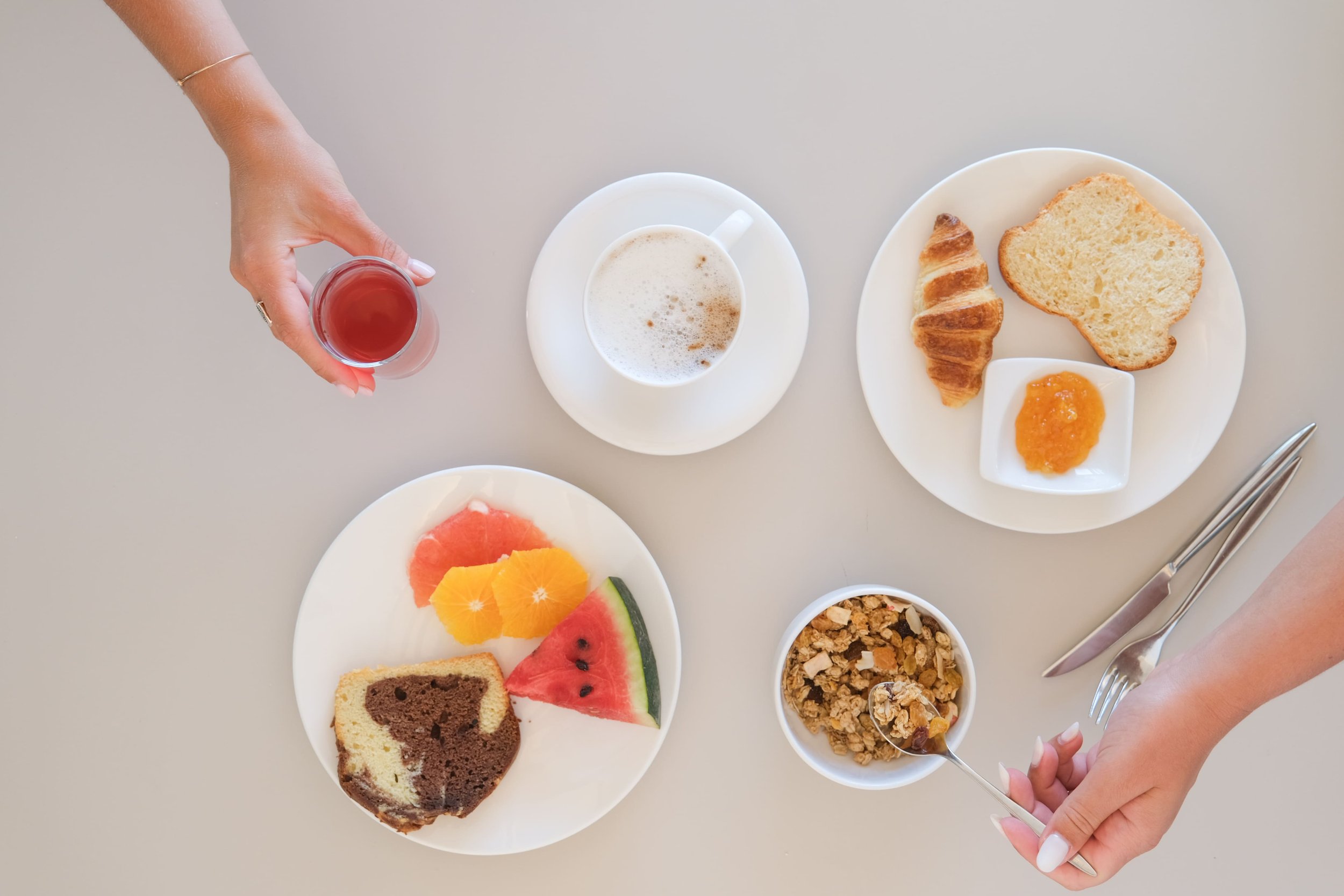 Une table de petit-déjeuner avec une main qui attrape une boisson et une autre main qui prend des céréales dans un bol.