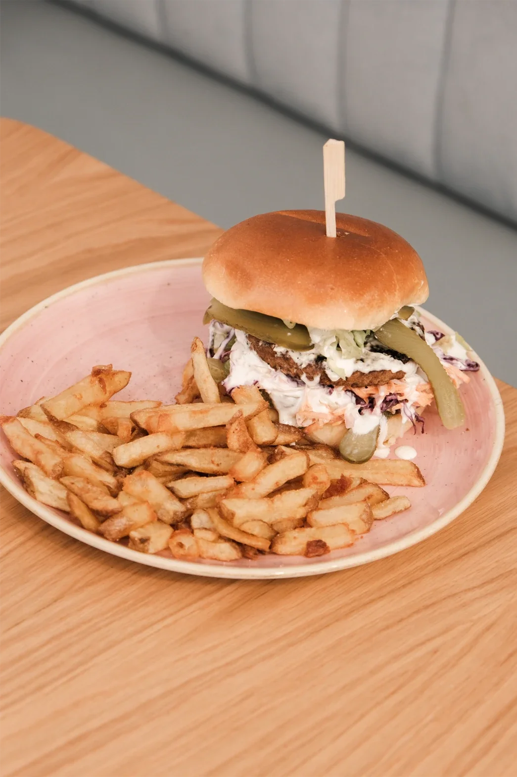 Un burger avec des frites sur une assiette rose.
