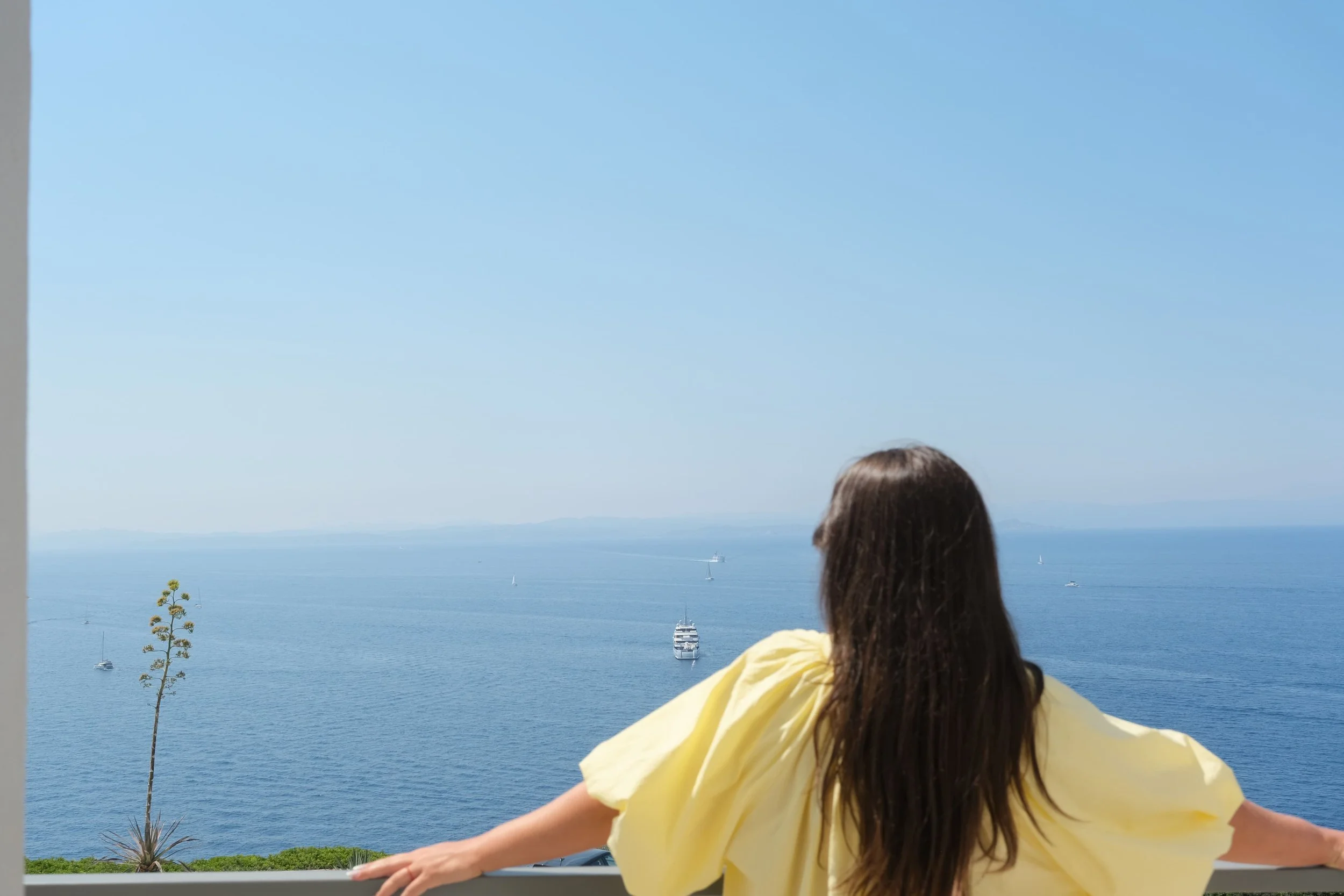 Une personne de dos qui regarde vers la mer, elle porte une robe jaune. 