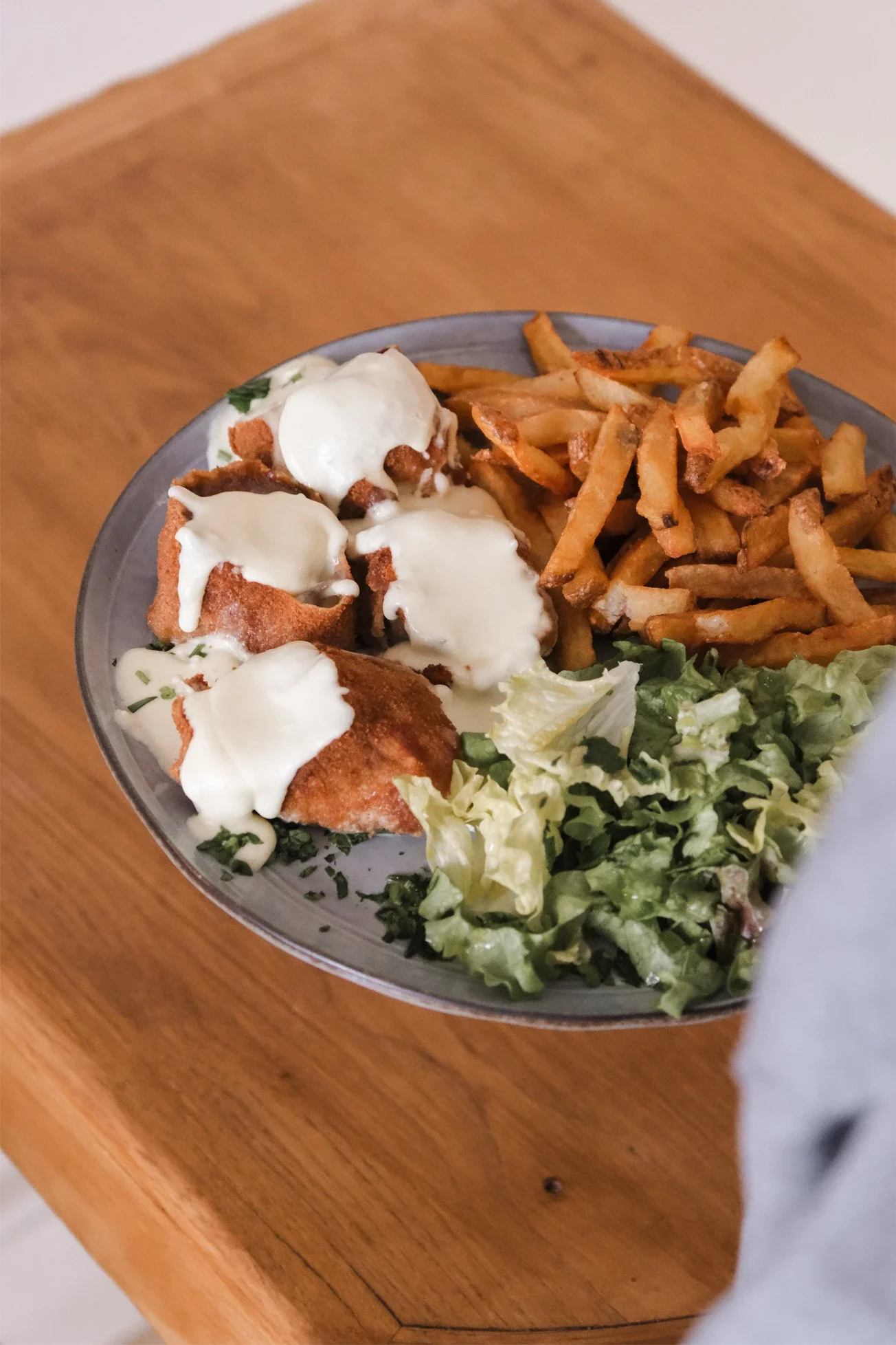 Assiette avec des frites, de la salade verte et des morceaux de poulet frits recouverts de sauce blanche.