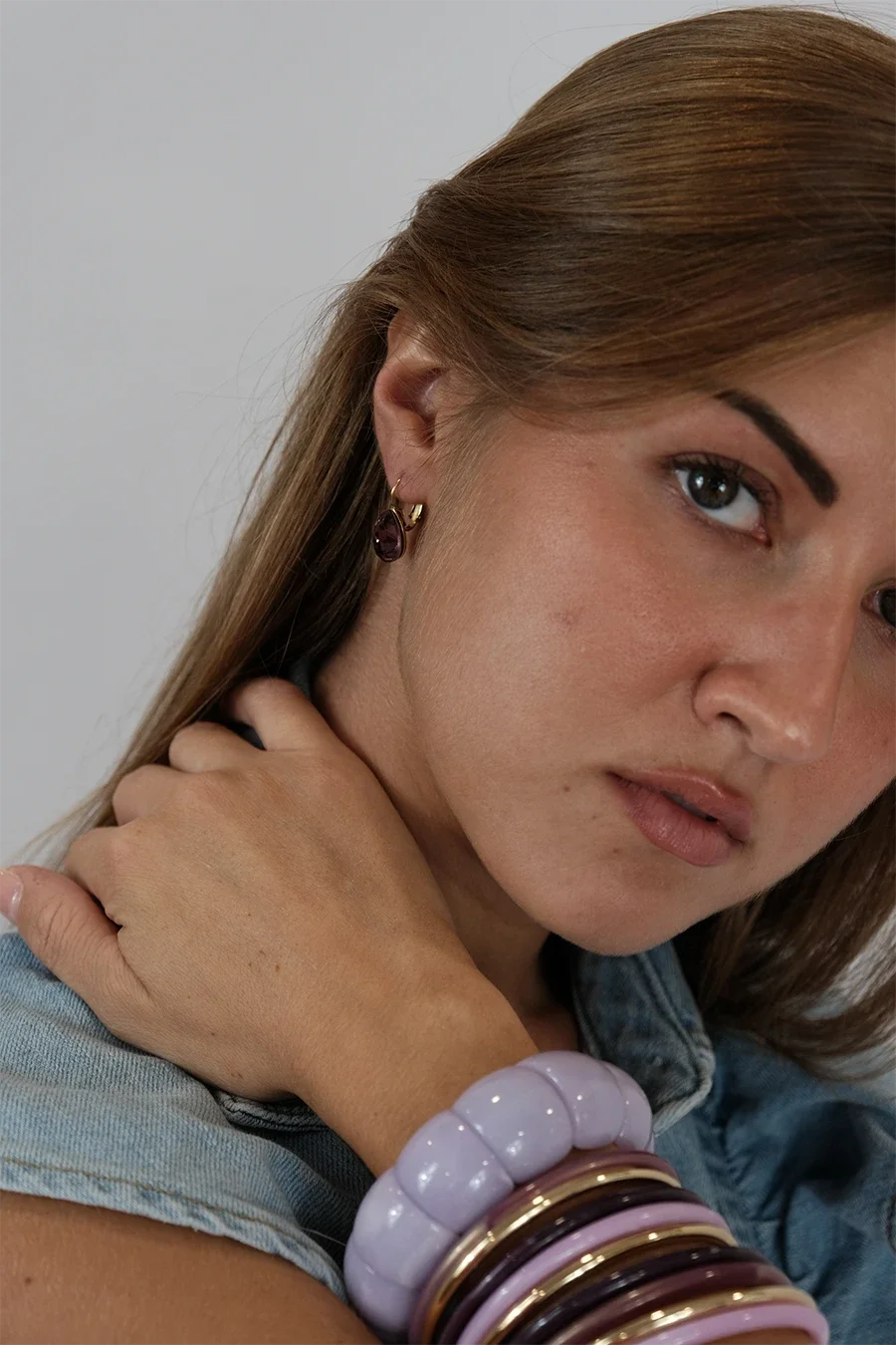 Jeune femme avec des boucles d'oreilles en or, bracelets en plastique violet et bracelets en métal, portant un jean.