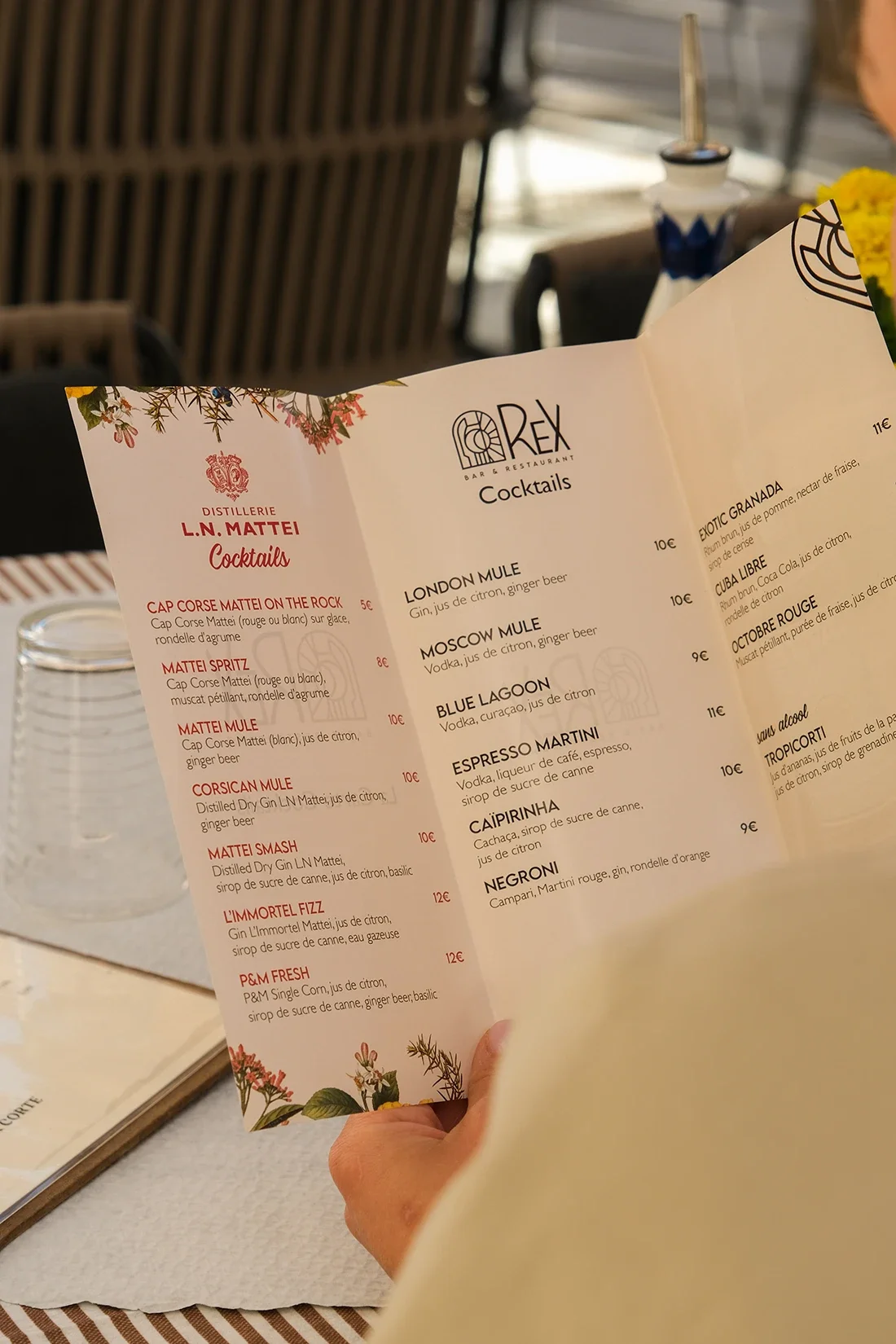 Une carte de menu de cocktails dans un restaurant, avec des noms de cocktails comme London Mule, Moscow Mule, Blue Lagoon, Espresso Martini, Caipirinha, etc.