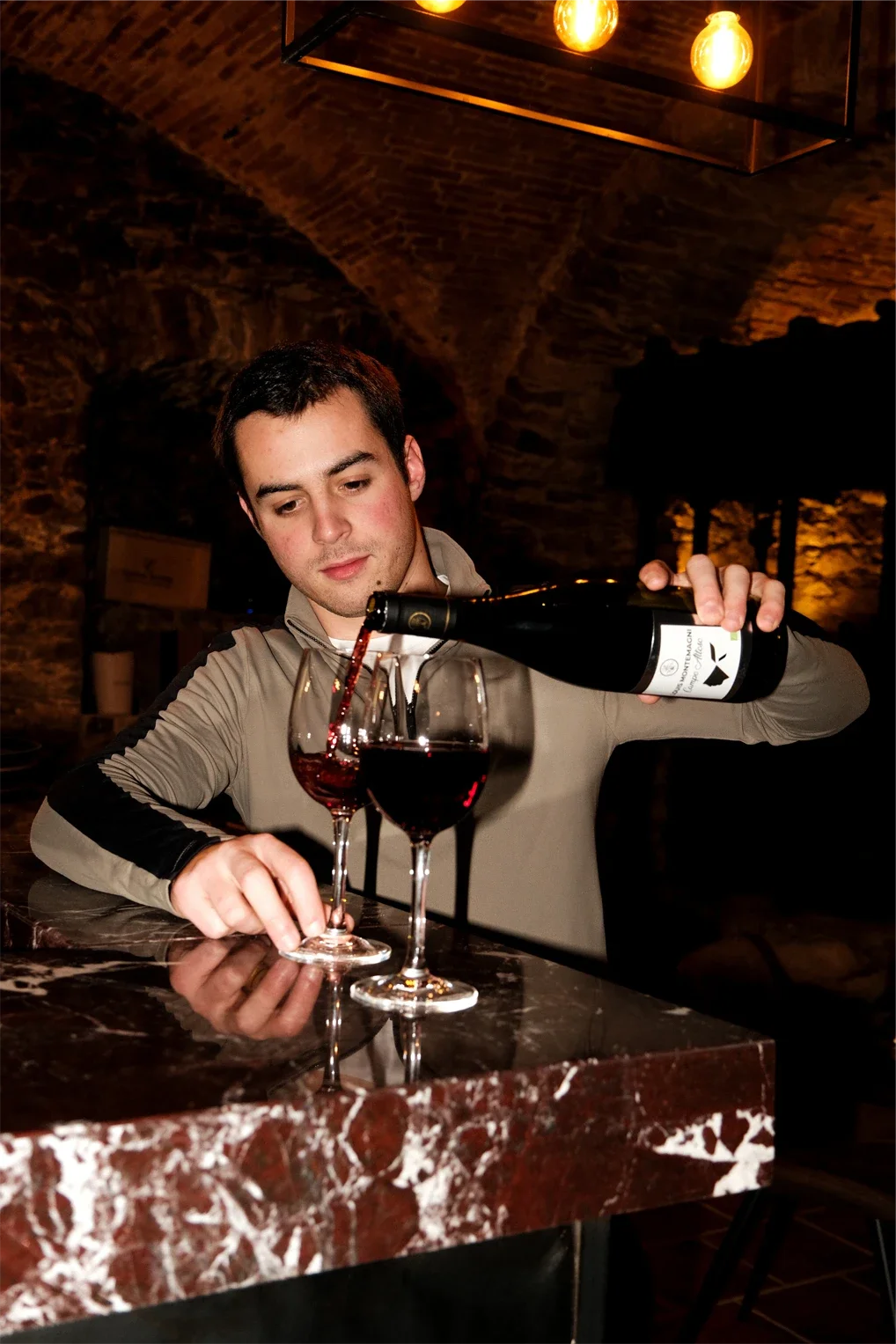 Homme servant du vin rouge dans un verre dans un bar ou restaurant avec un décor en pierre