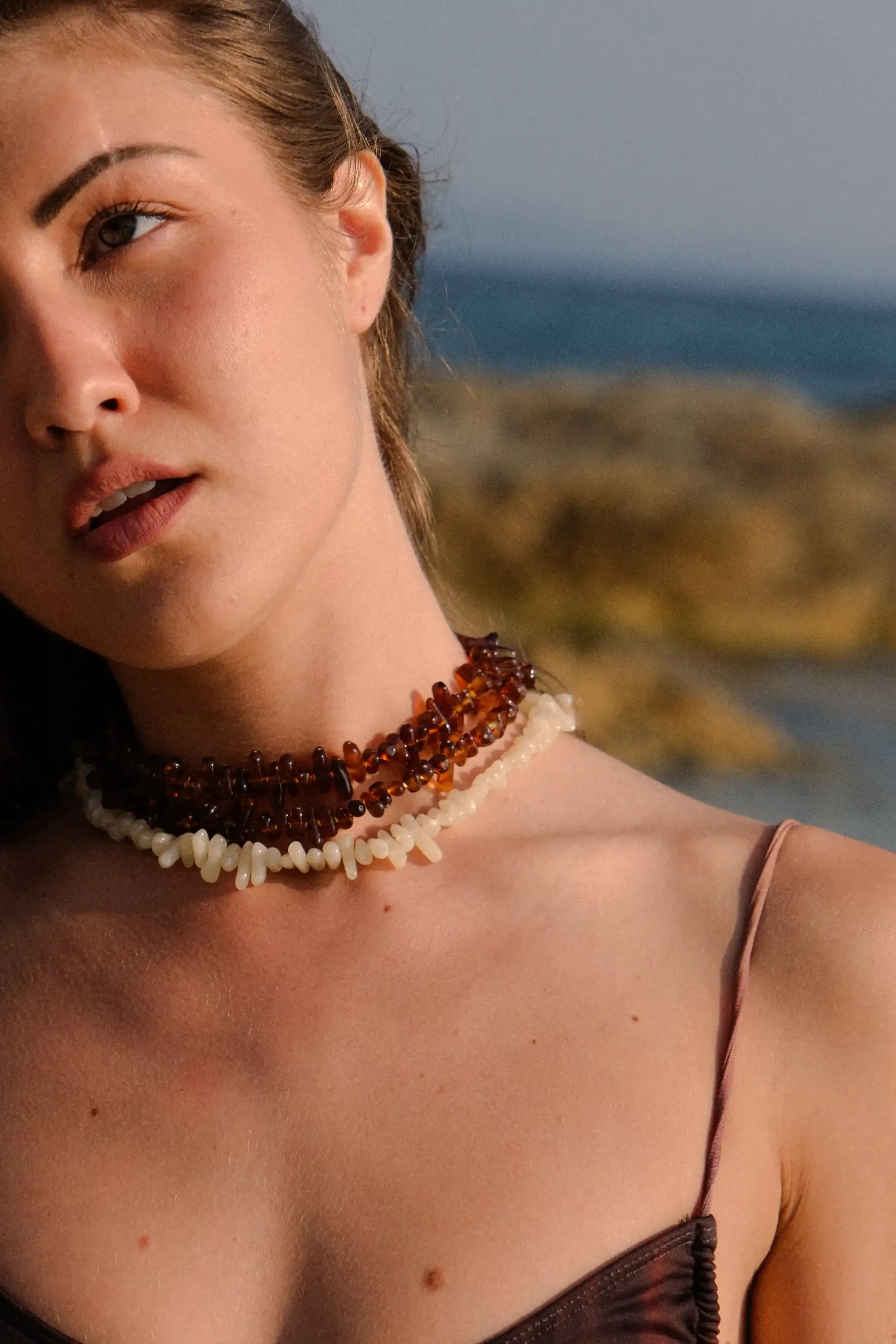 Photo d'une femme portant des colliers en perles, avec une plage et la mer en arrière-plan.
