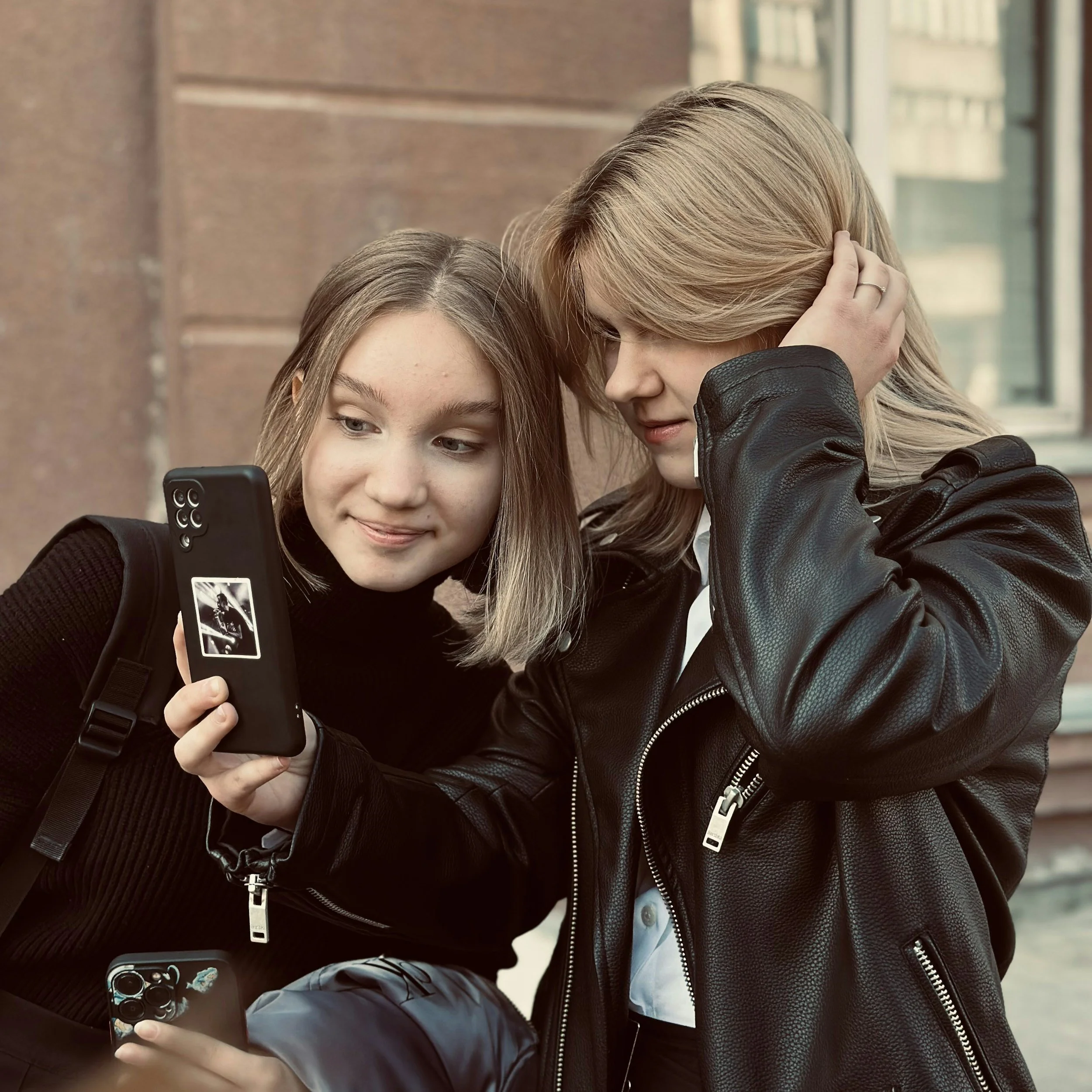Two young women looking at a phone together outdoors.