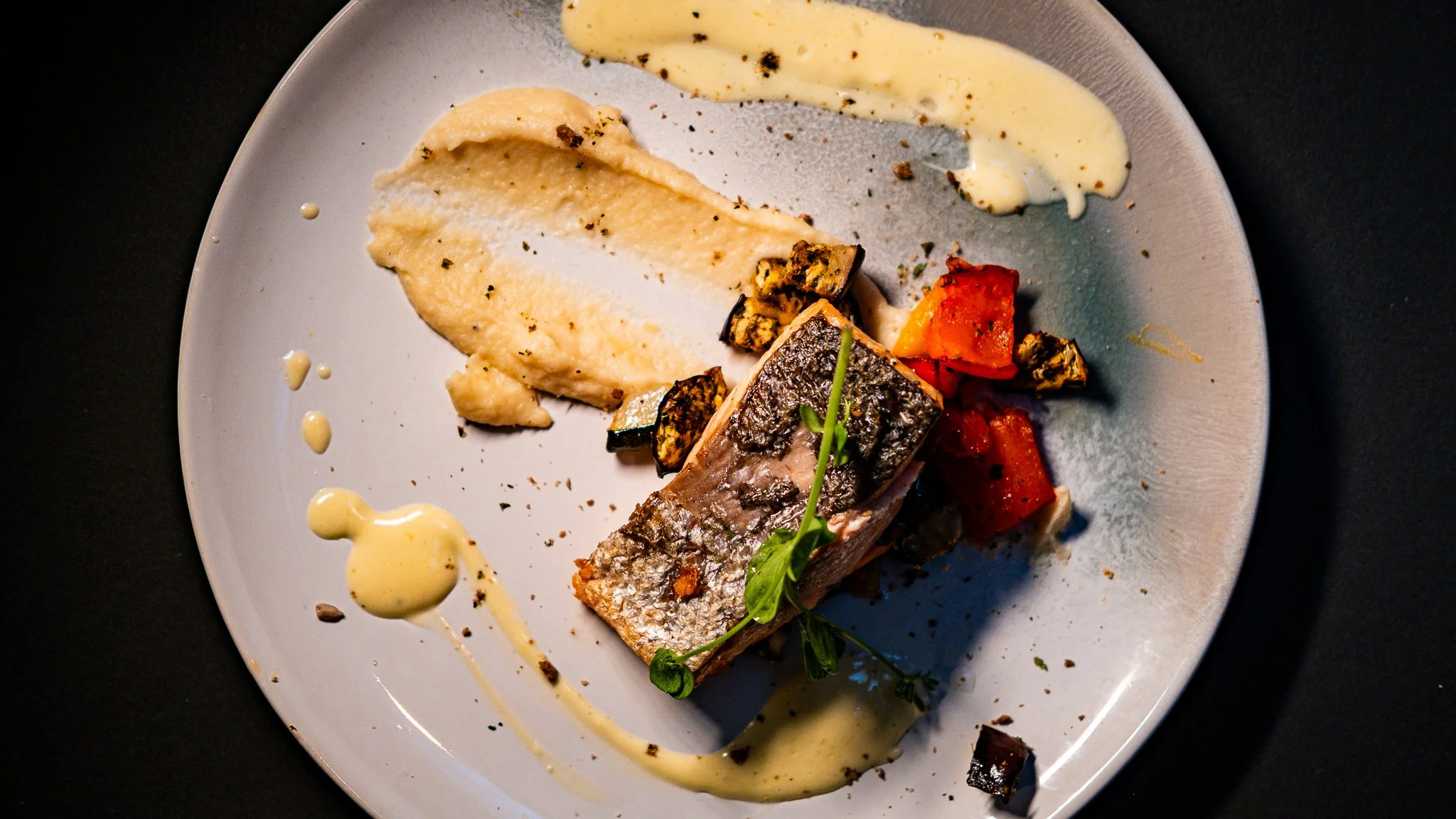 Fish fillet served with purée, vegetables and creamy sauce on a grey plate.