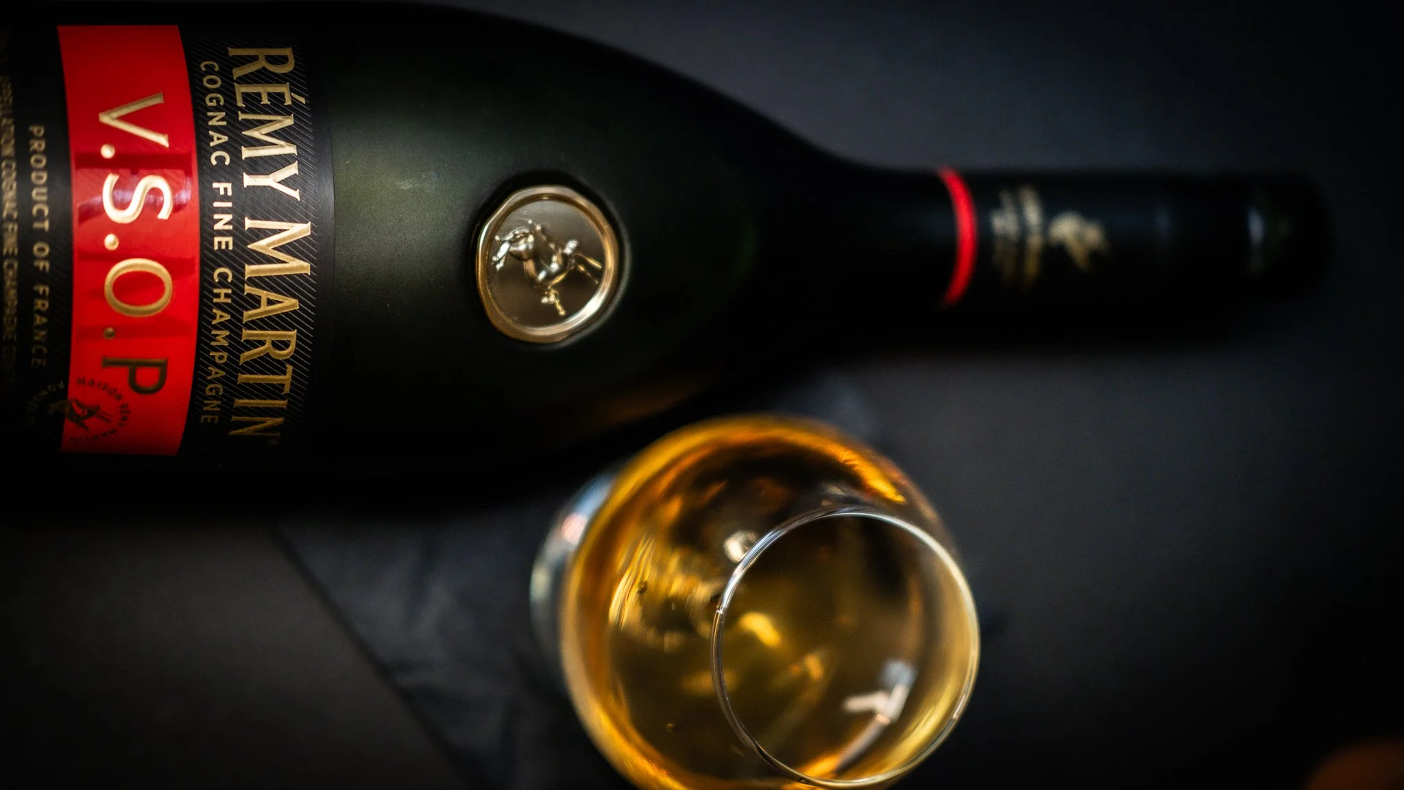 Rémy Martin V.S.O.P cognac bottle beside a glass of cognac on a dark surface.