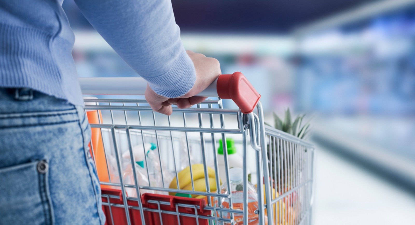 Person pushing a shopping cart filled with groceries in a store aisle.
