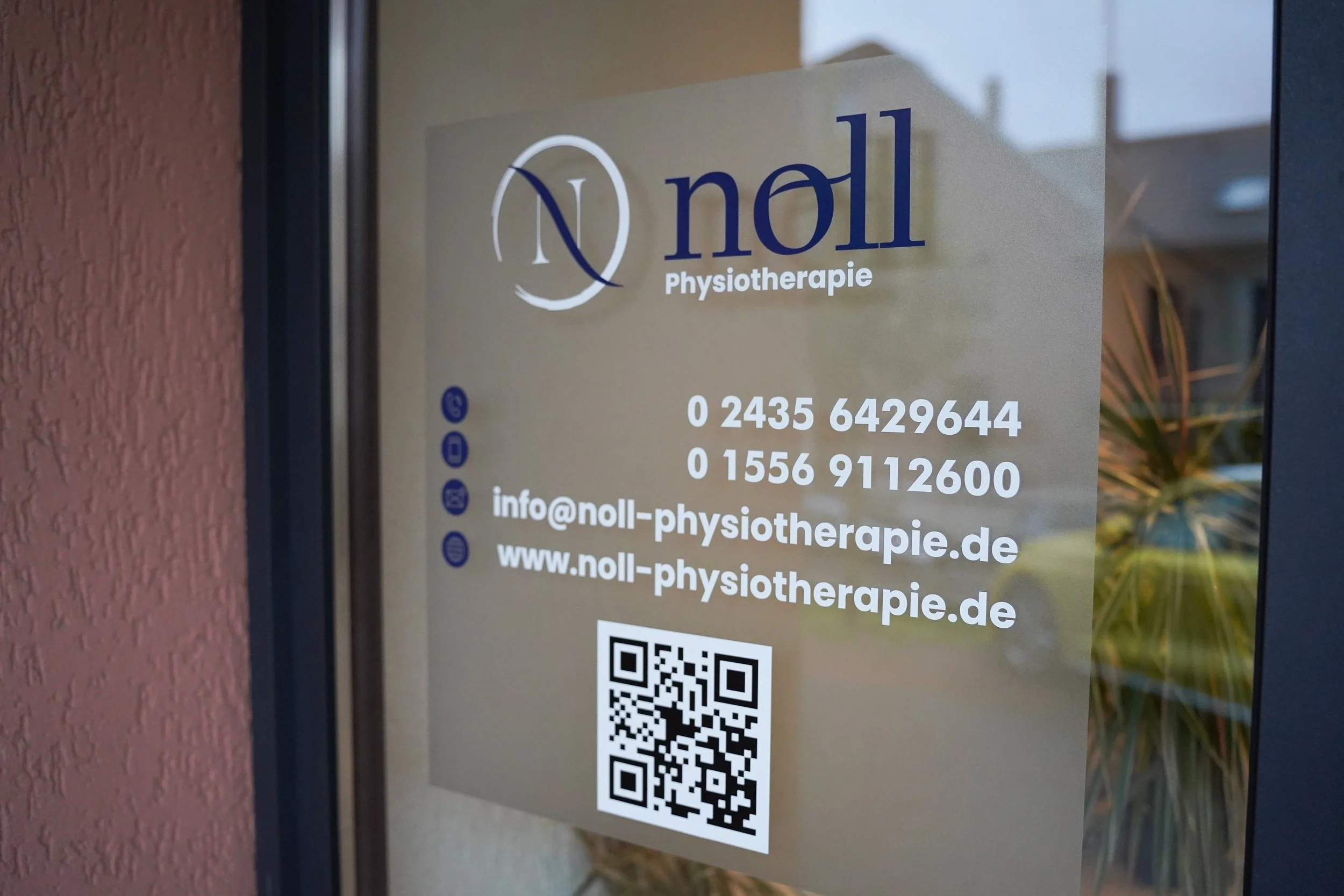 Aufkleber an einer Tür mit Logo, Kontaktinformationen und QR-Code für eine Physiotherapie-Praxis namens Noll.