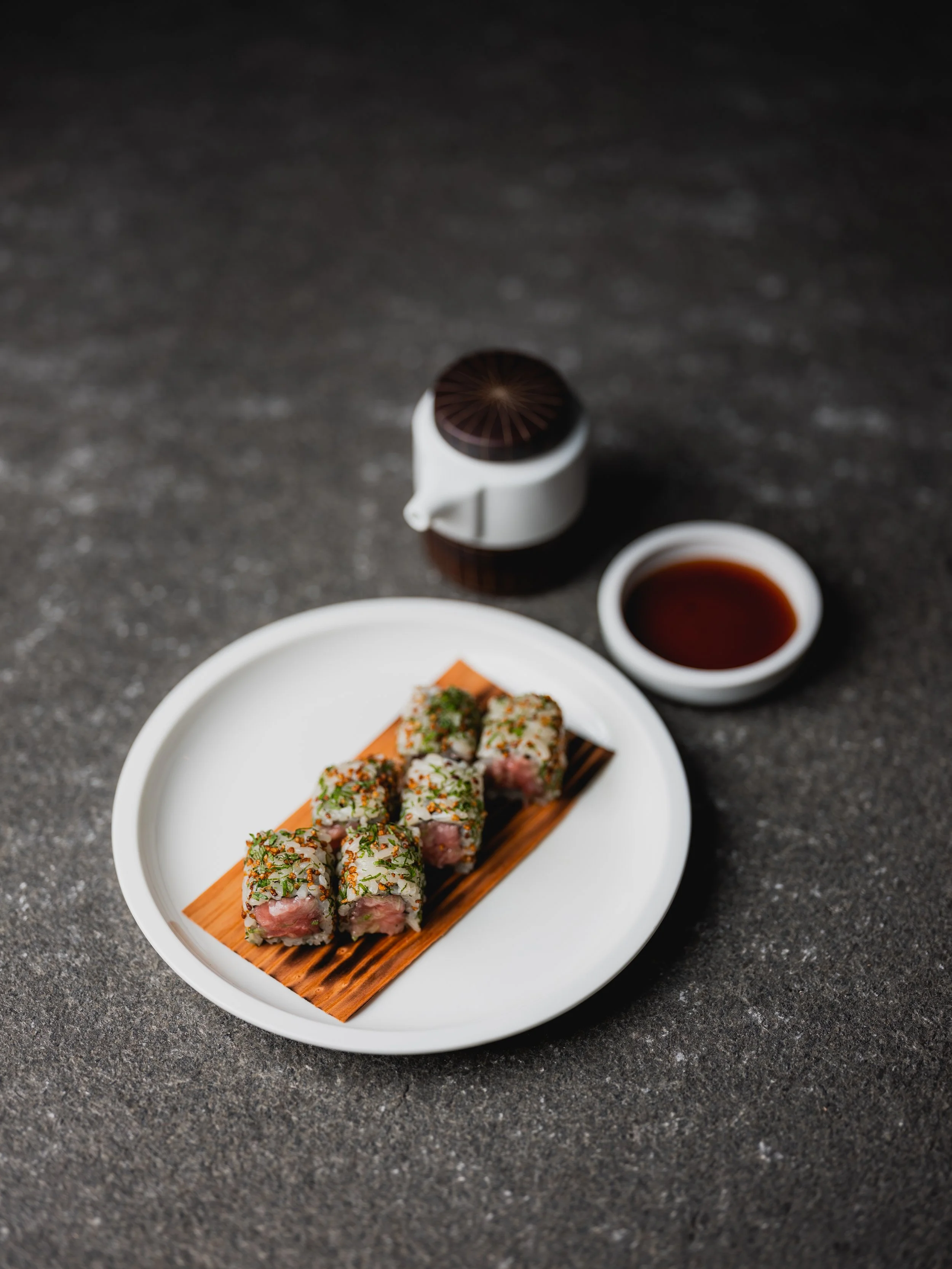 Rotolo di tonno su piatto bianco con salsa di soia a parte.