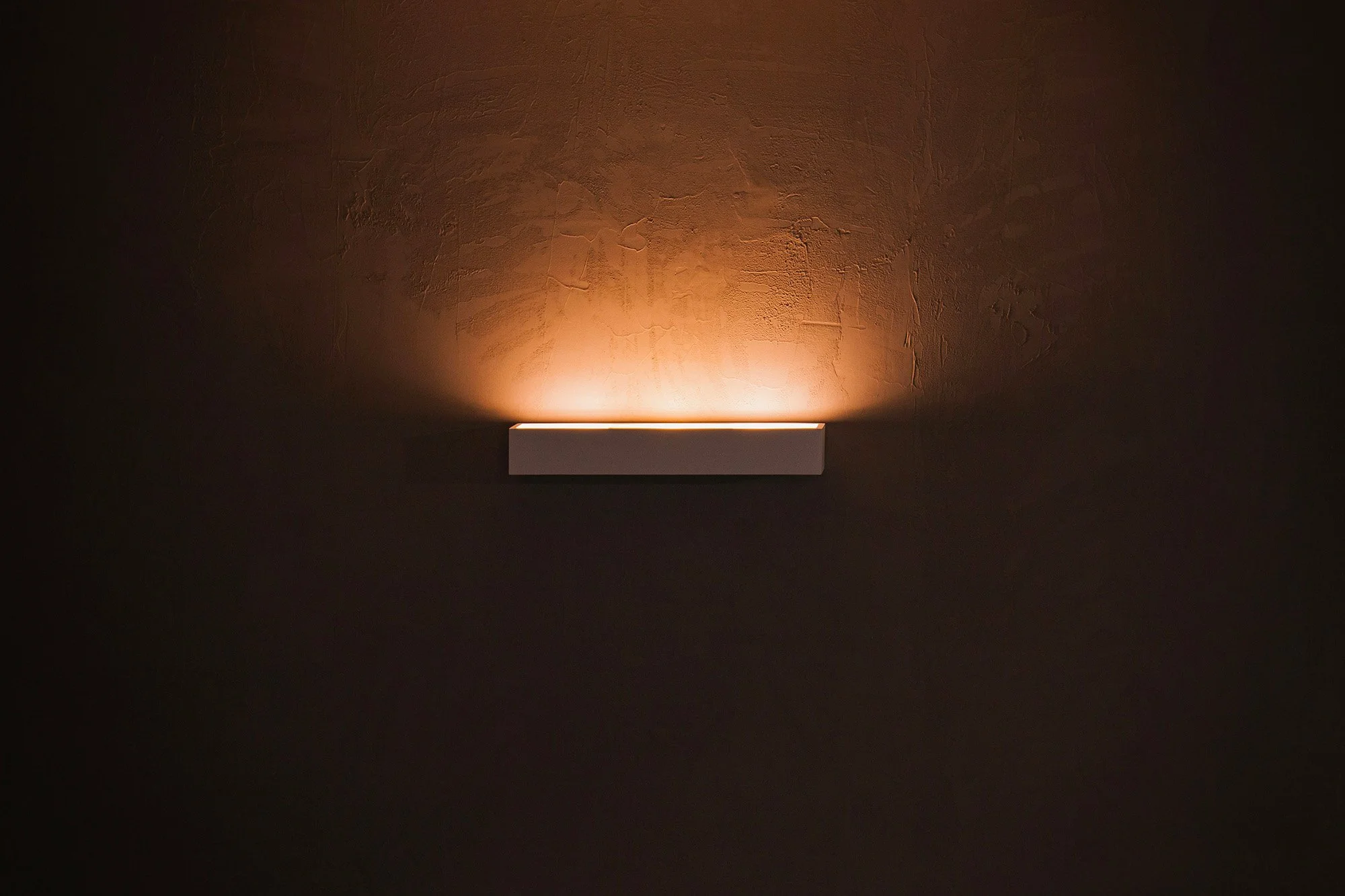 Lustre moderne blanc fixée au plafond, émettant une lumière chaude, dans un espace sombre.
