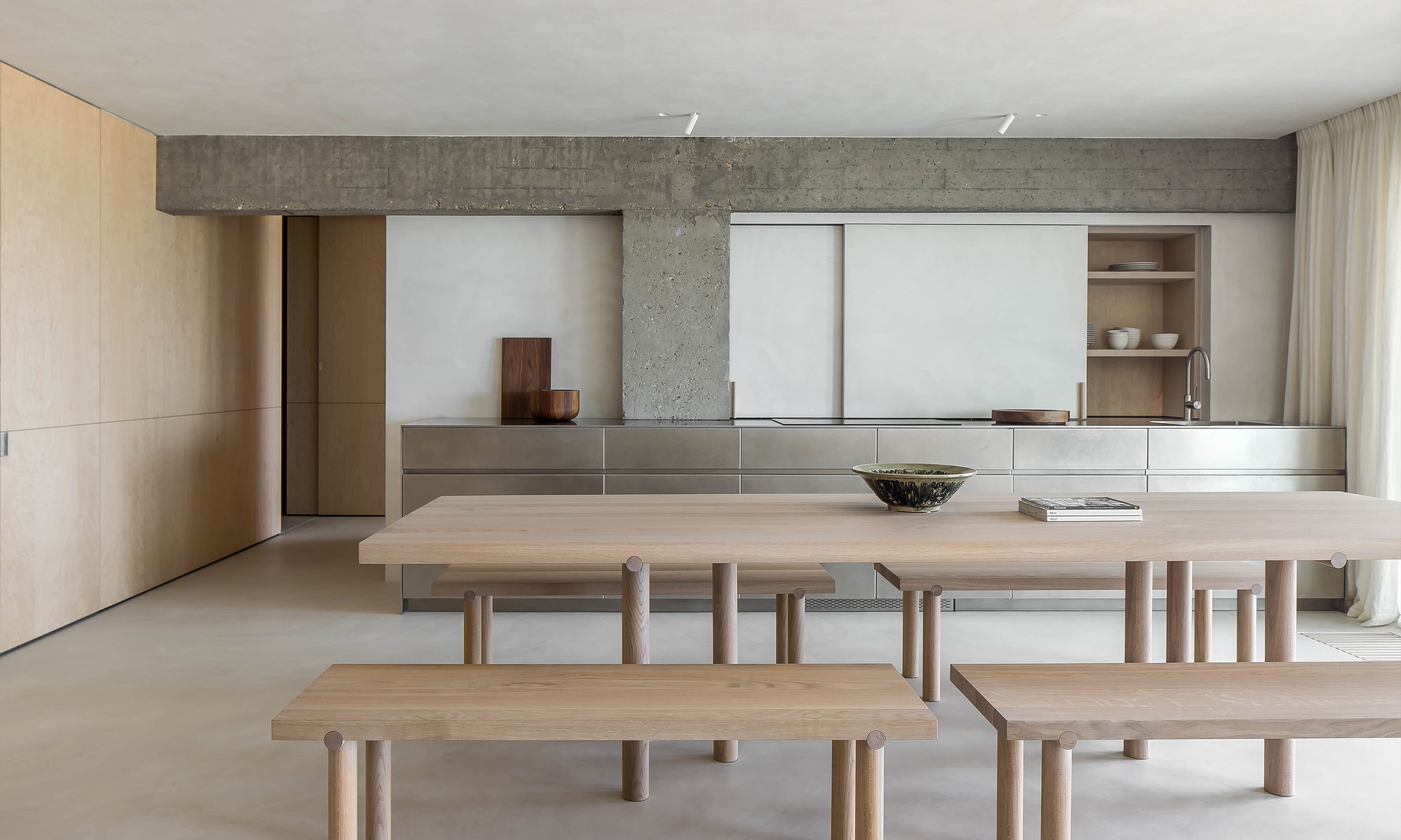Cuisine moderne avec mobilier en bois clair, étagères ouvertes avec vaisselle blanche, comptoir en métal, grand surface de travail, bowl décoratif, et rideaux blancs.