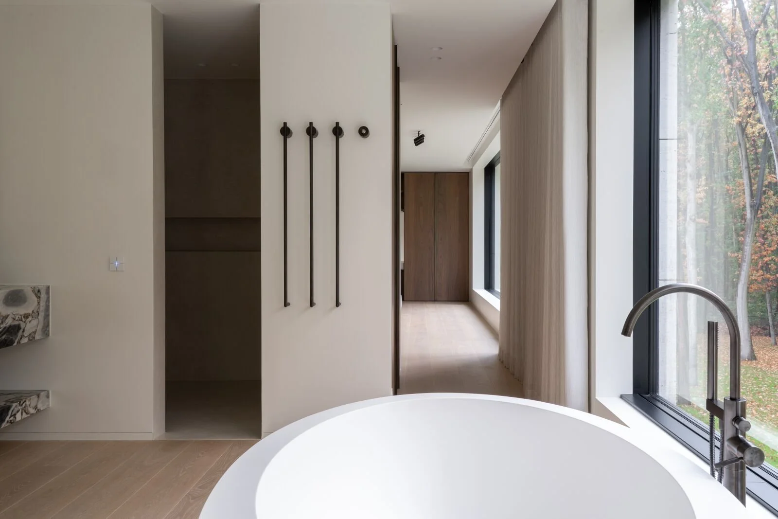 Vue intérieure d'une salle de bain moderne avec une grande fenêtre laissant entrer la lumière naturelle, un évier en marbre, et un baignoire ronde blanche.