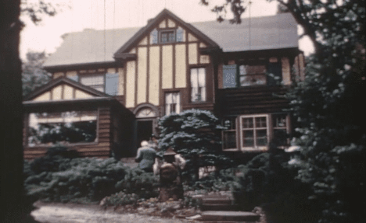 A large, two-story house with a Tudor-style exterior, surrounded by trees and shrubs in a garden.
