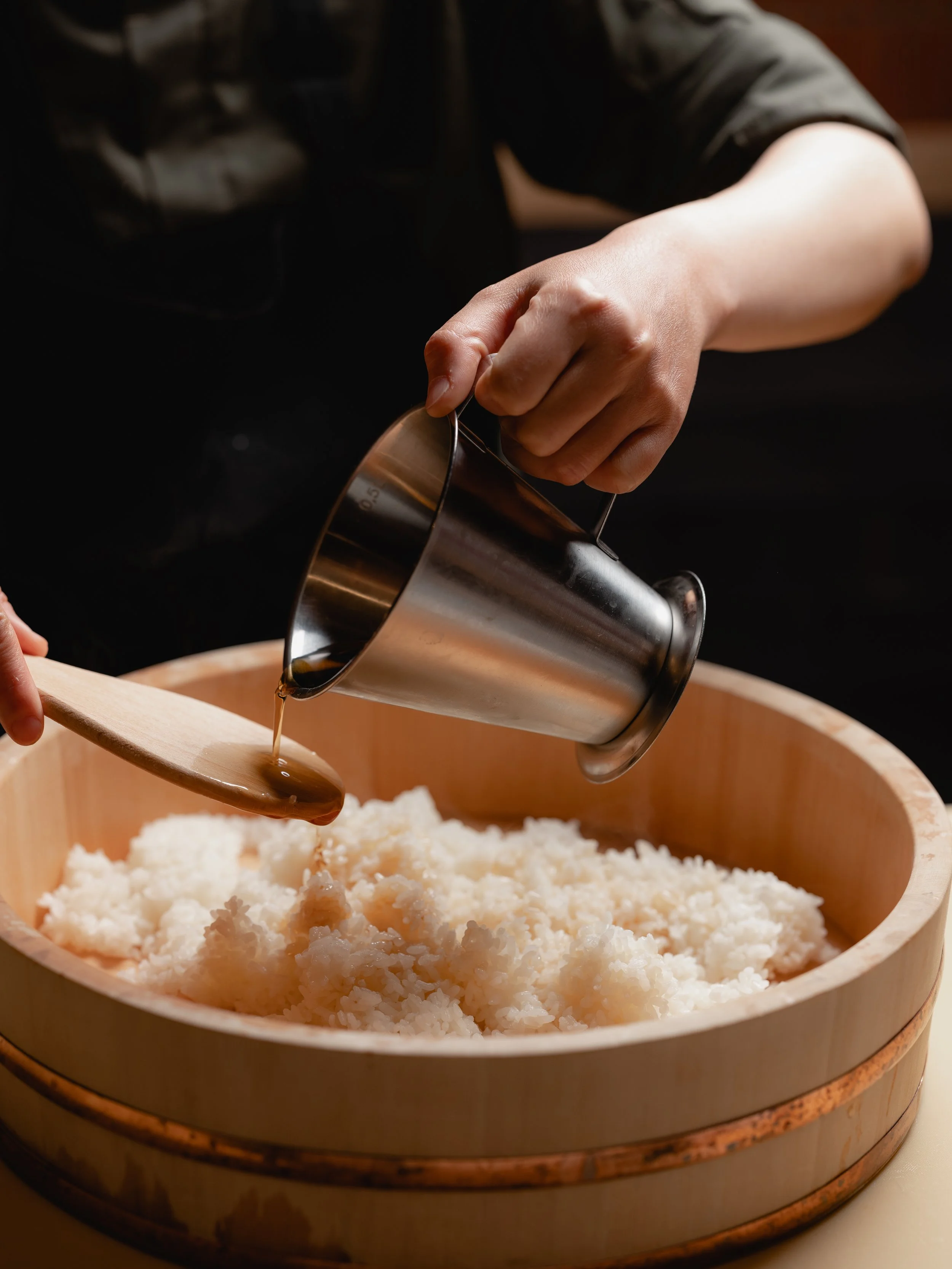 寿司桶の中でご飯と酢を混ぜる寿司職人⁠。