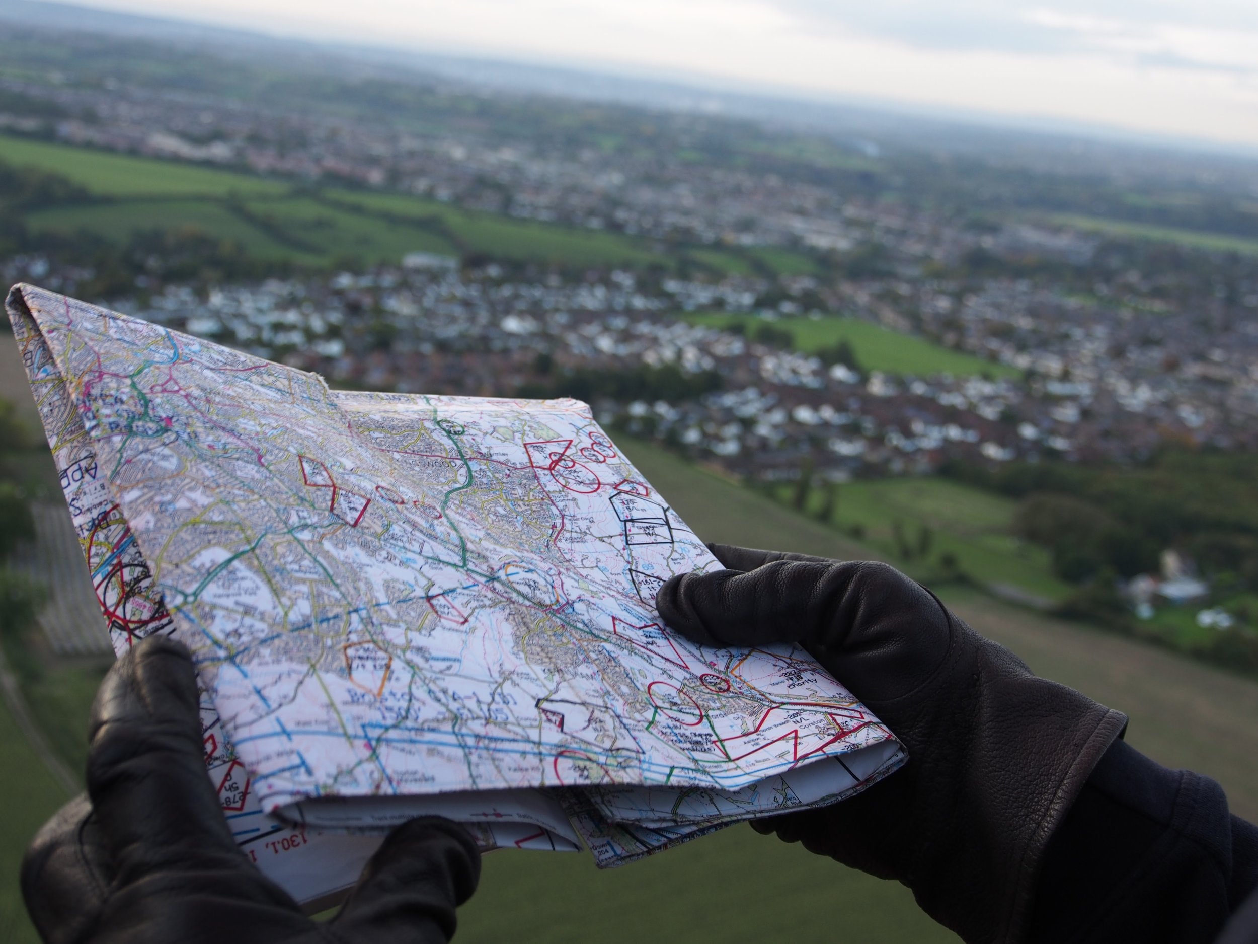 A pair of gloved hands holding a map, with the view from a balloon in the background
