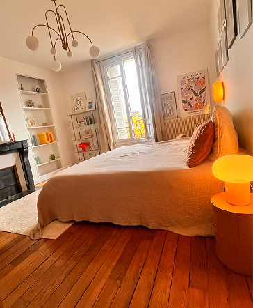 Anne Bassam - Chambre moderne avec lit, lampes orange, étagères, œuvres d'art au mur et grande fenêtre.